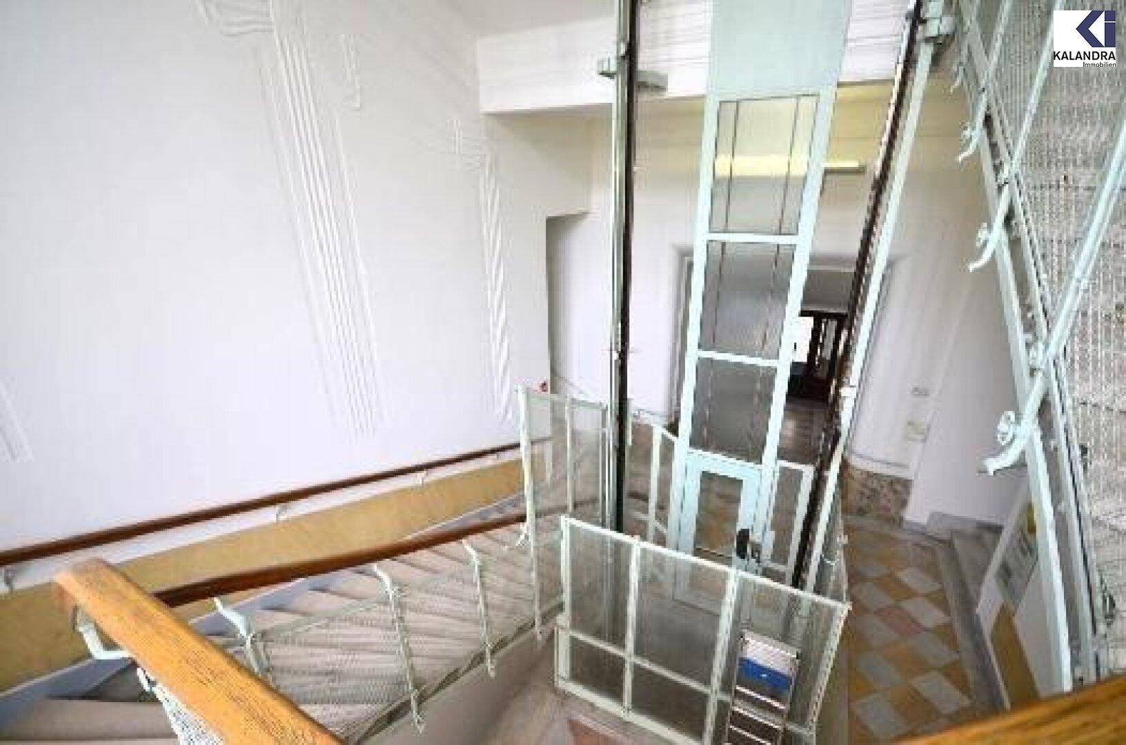 Detailansicht des Treppenhauses mit einem modernen Glasaufzug und kunstvollen Geländern.