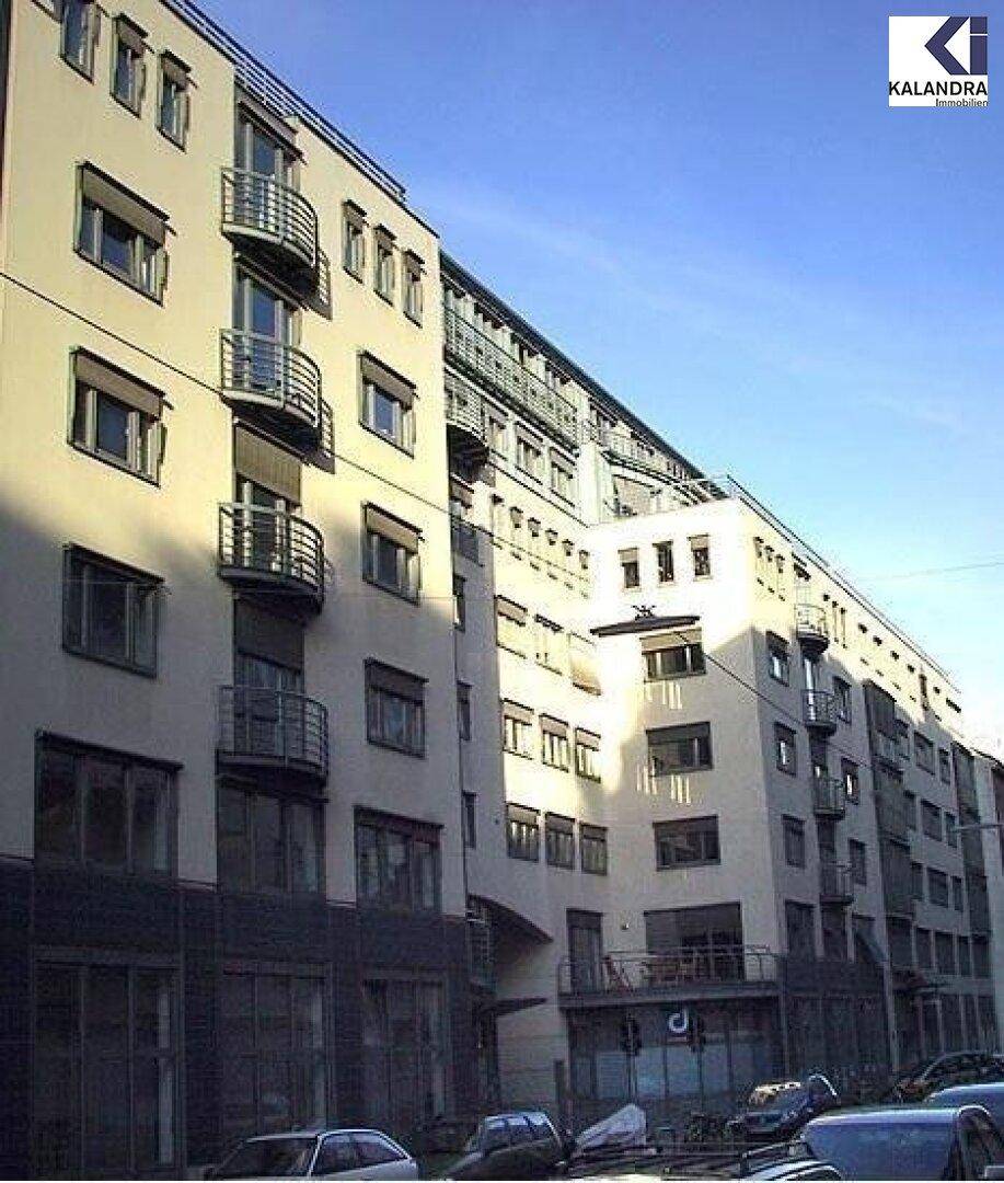 Mehrere Gebäude mit Balkonen und großen Fenstern entlang einer städtischen Straße bei Sonnenschein.