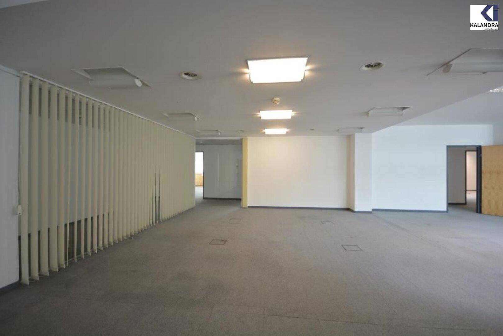 Großes, offenes Büro mit Teppichboden und vertikalen Jalousien, bereit für die individuelle Gestaltung und flexible Nutzung.