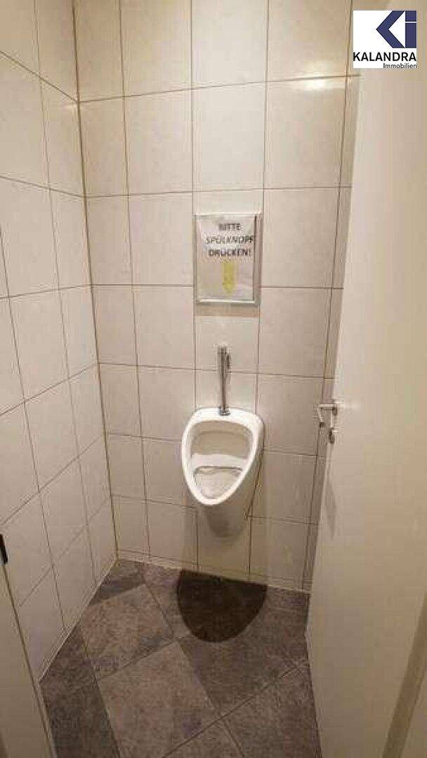 Toilettenraum mit weißen Fliesen, Urinal und dunklem Fliesenboden, sehr gepflegt.