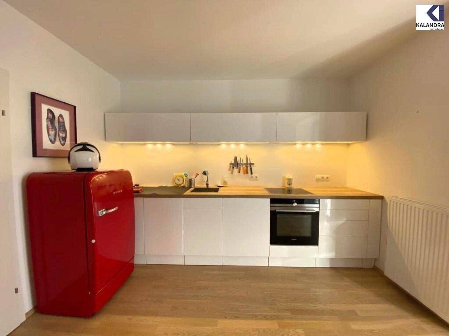 Moderne Einbauküche mit weißen Schränken, Holztheke und rotem Kühlschrank.