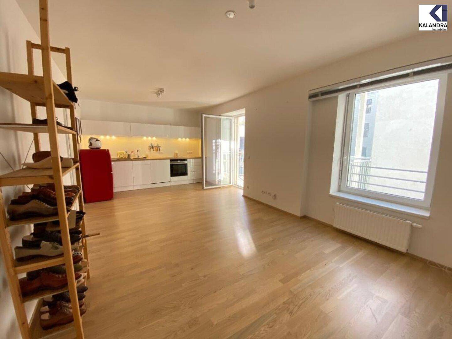 Geräumiger Wohnbereich mit offener Küche, Parkettboden und großem Fenster.
