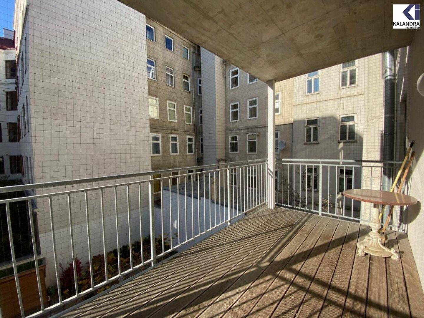 Überdachter Balkon mit Holzboden und kleinem Tisch, Blick auf den Innenhof.