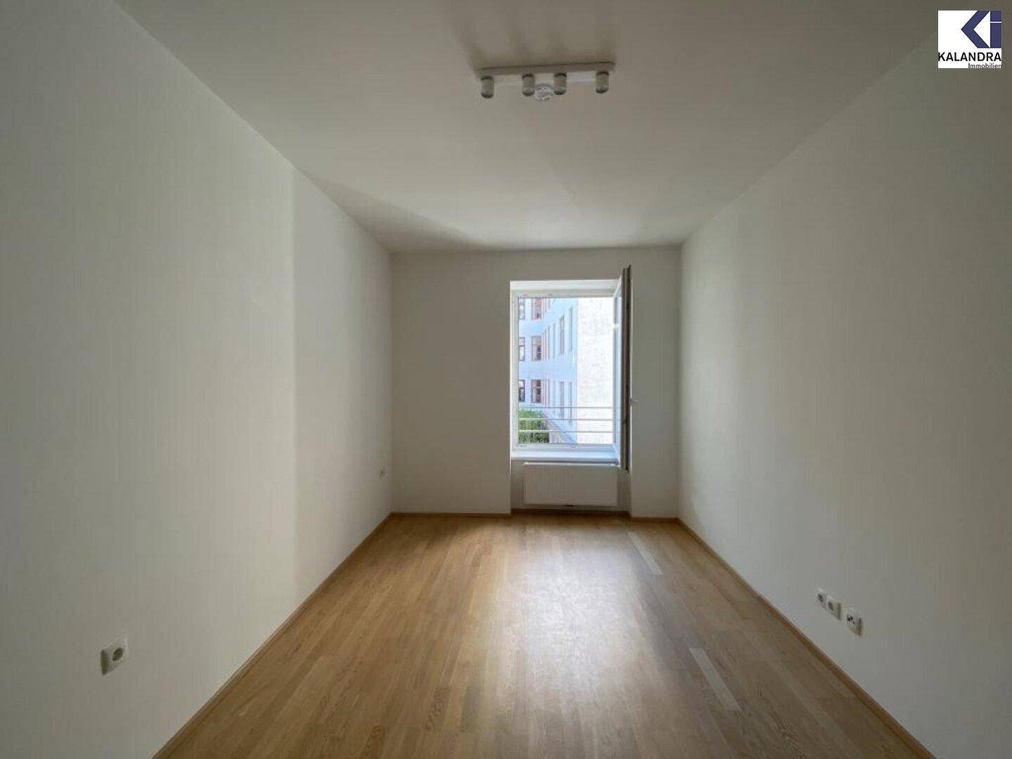 Leeres Zimmer mit Parkettboden und großem Fenster, ideal als Schlafzimmer.