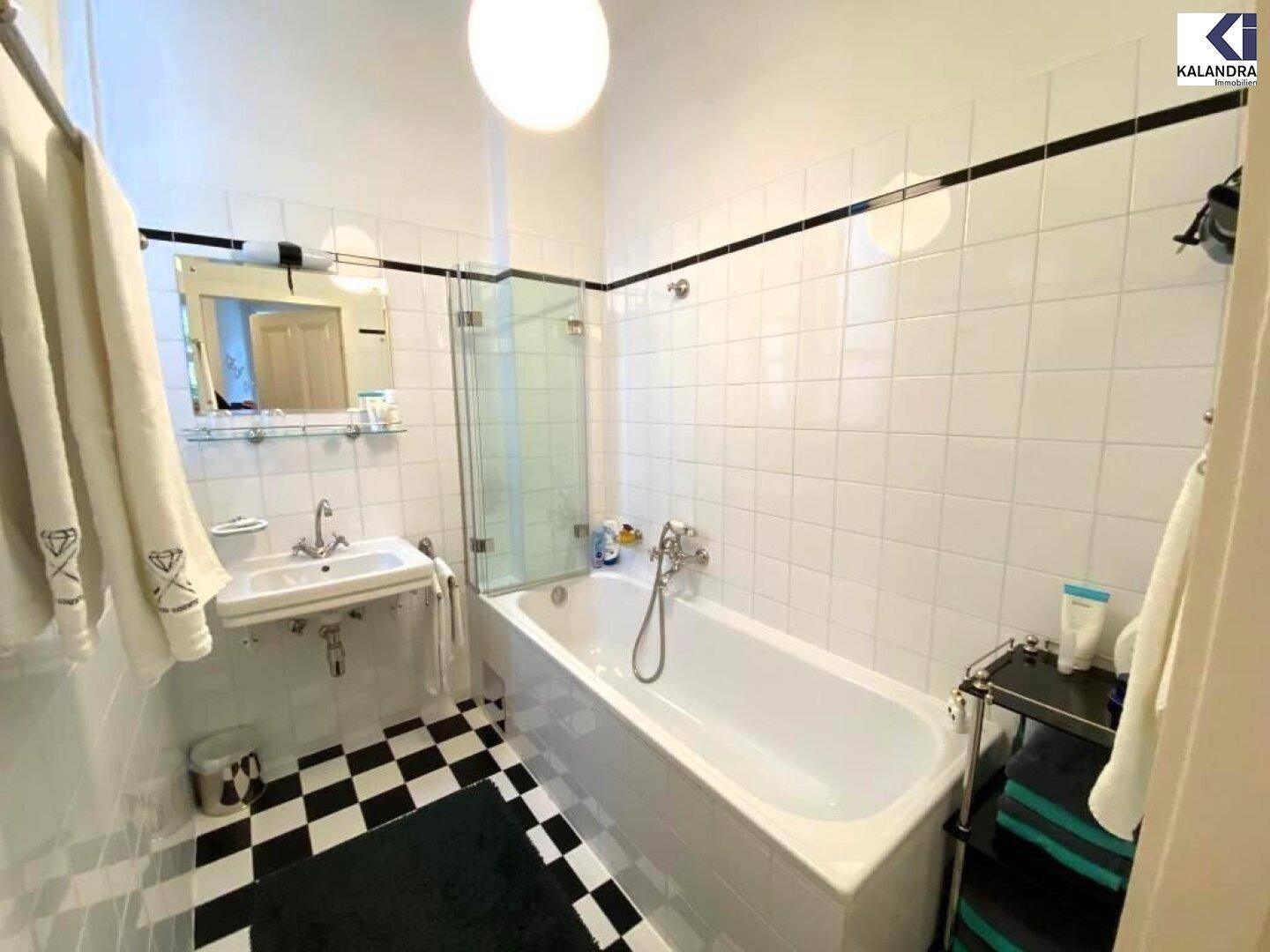 Funktionales Badezimmer mit Badewanne, Duschabtrennung und Waschbecken, ausgestattet mit schwarz-weißem Fliesenboden.