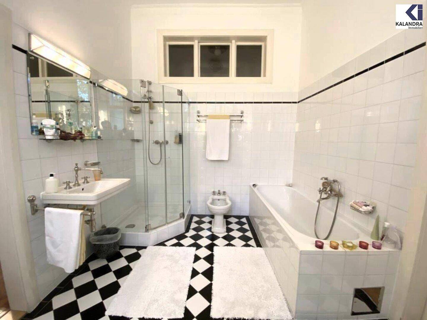 Helles Badezimmer mit schwarz-weiß karierten Fliesen, Badewanne, Dusche und Bidet.