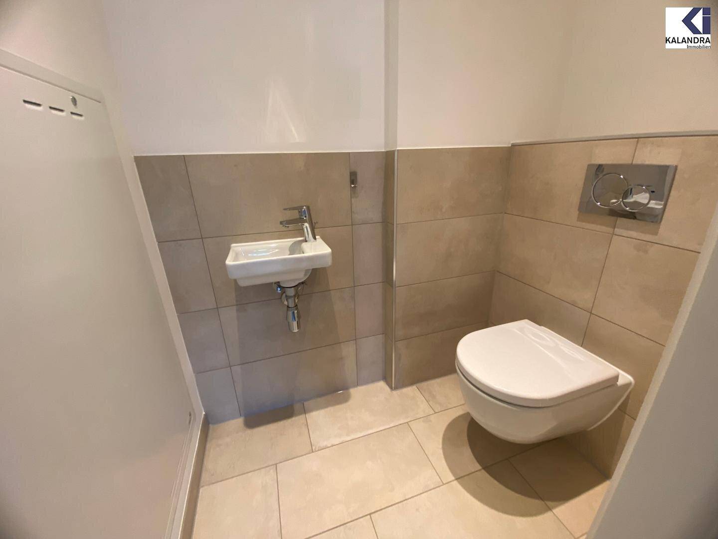 Modernes Gäste-WC mit Wand-WC und kleinem Handwaschbecken, hell gefliest.