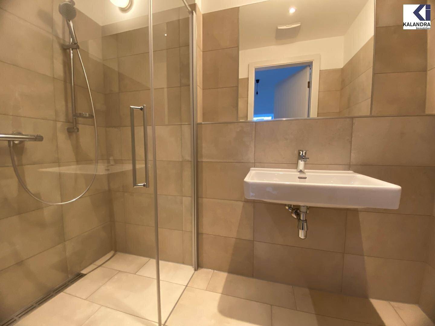 Modernes Badezimmer mit Duschkabine und Waschbecken, hell gefliest und gut beleuchtet.