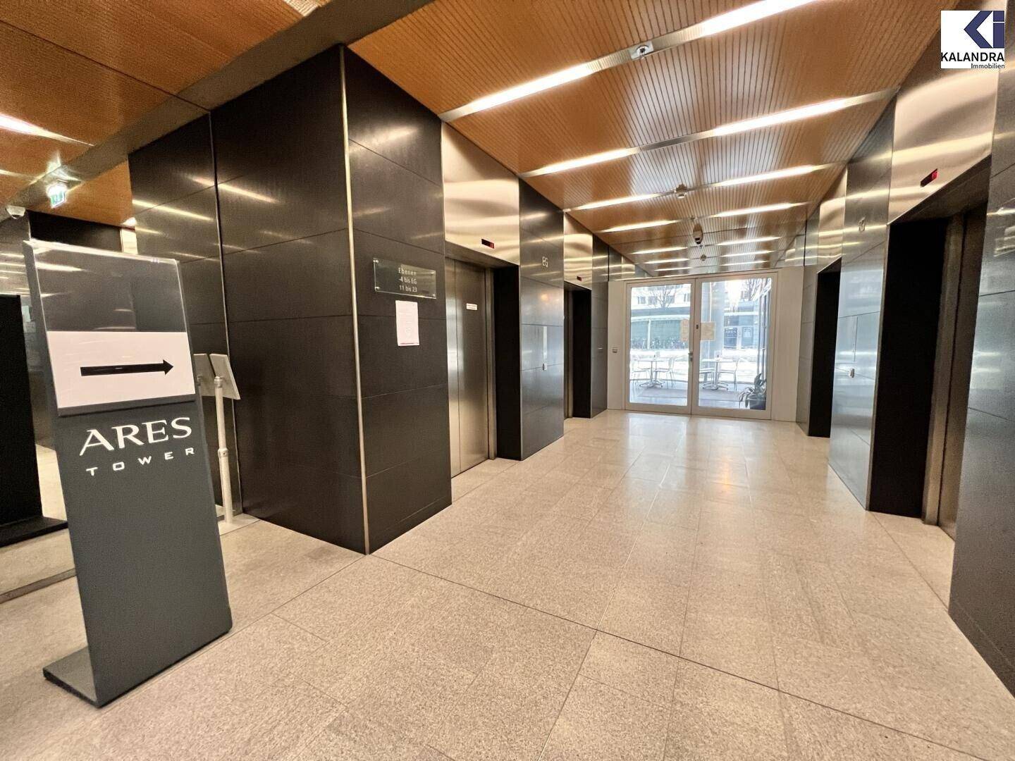 Moderne und geräumige Lobby mit mehreren Aufzügen, hellem Fliesenboden und einem Hinweisschild für den Ares Tower.