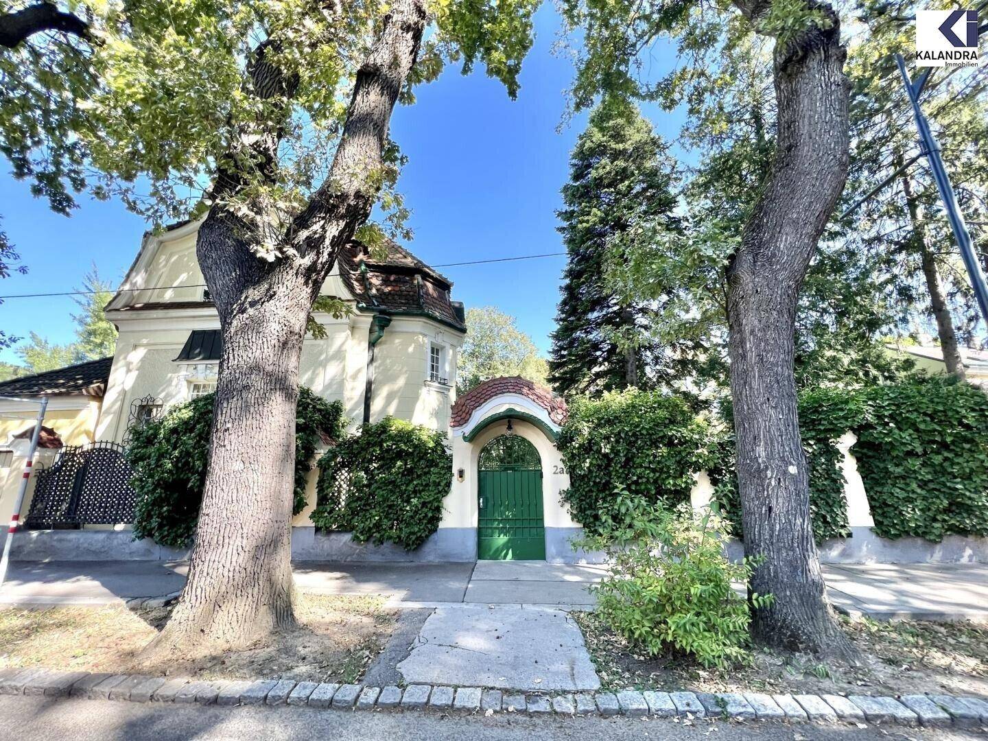 Historisches Eingangstor zur Villa, umgeben von Bäumen und gepflegter Vegetation an der Straße.