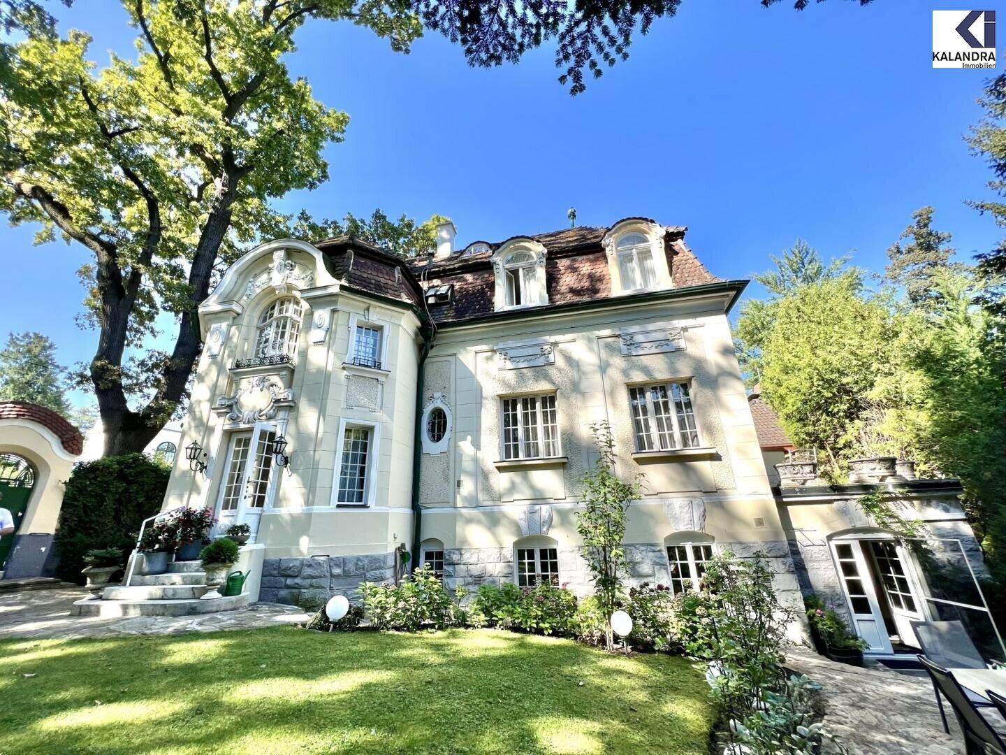 Prächtige Villa mit klassischer Architektur und weitläufigem Garten unter strahlend blauem Himmel.