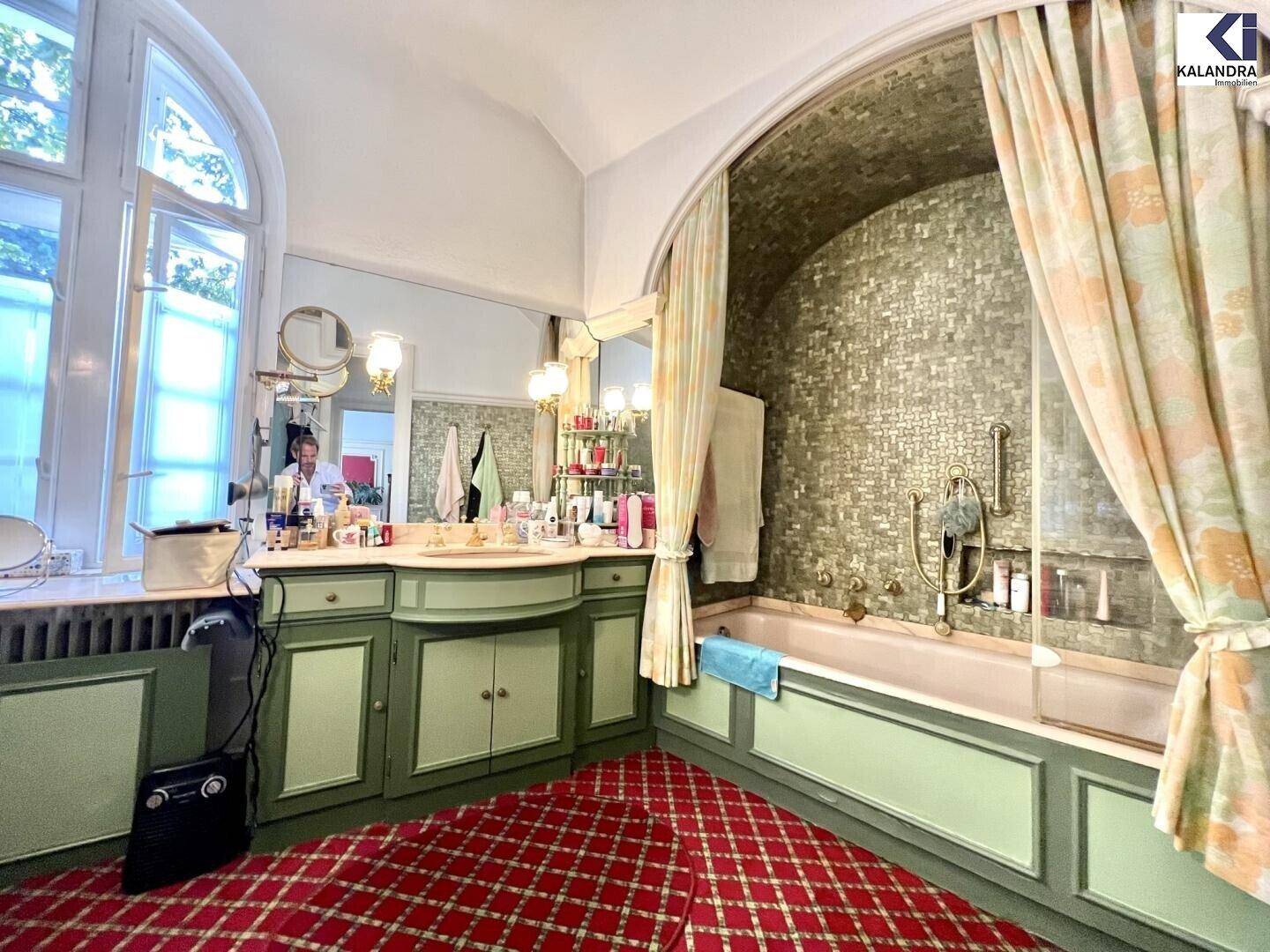 Historisches Badezimmer mit Badewanne, Mosaikfliesen und einem großen Fenster für Tageslicht.