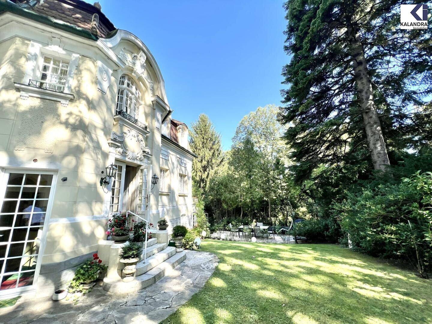 Weitläufiger Gartenbereich mit Rasenfläche und altem Baumbestand neben der eleganten Villa.