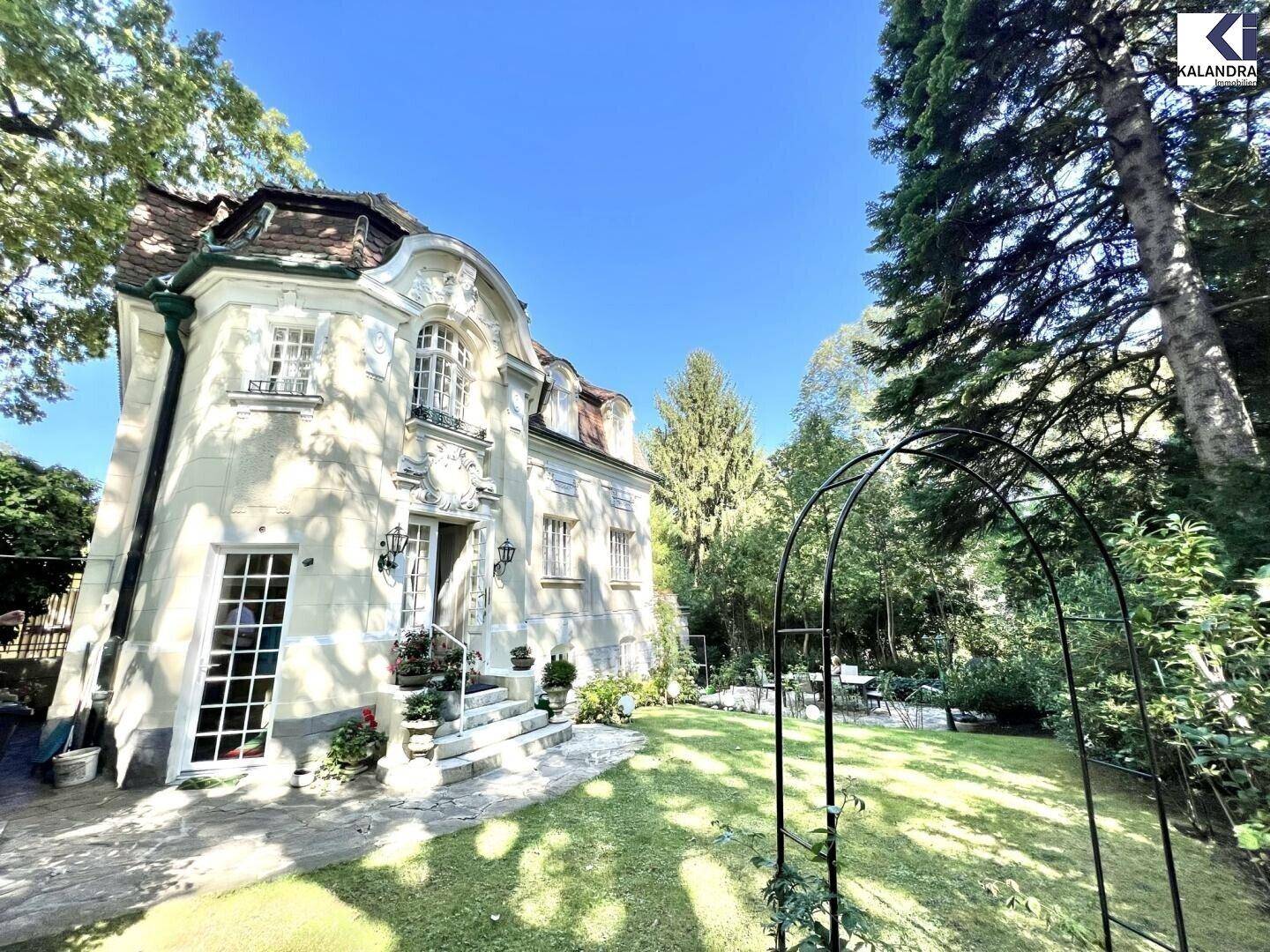 Gepflegter Garten mit Rasenfläche, dekorativem Bogen und Blick auf die historische Villa.