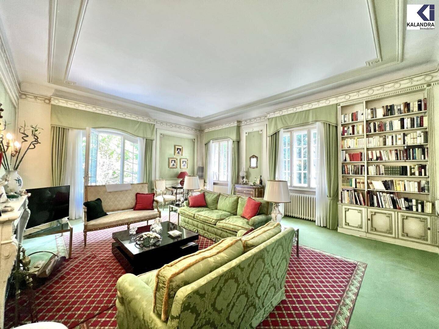 Geräumiges Wohnzimmer mit grünen Wänden, eleganten Sofas und einem großen Bücherregal.