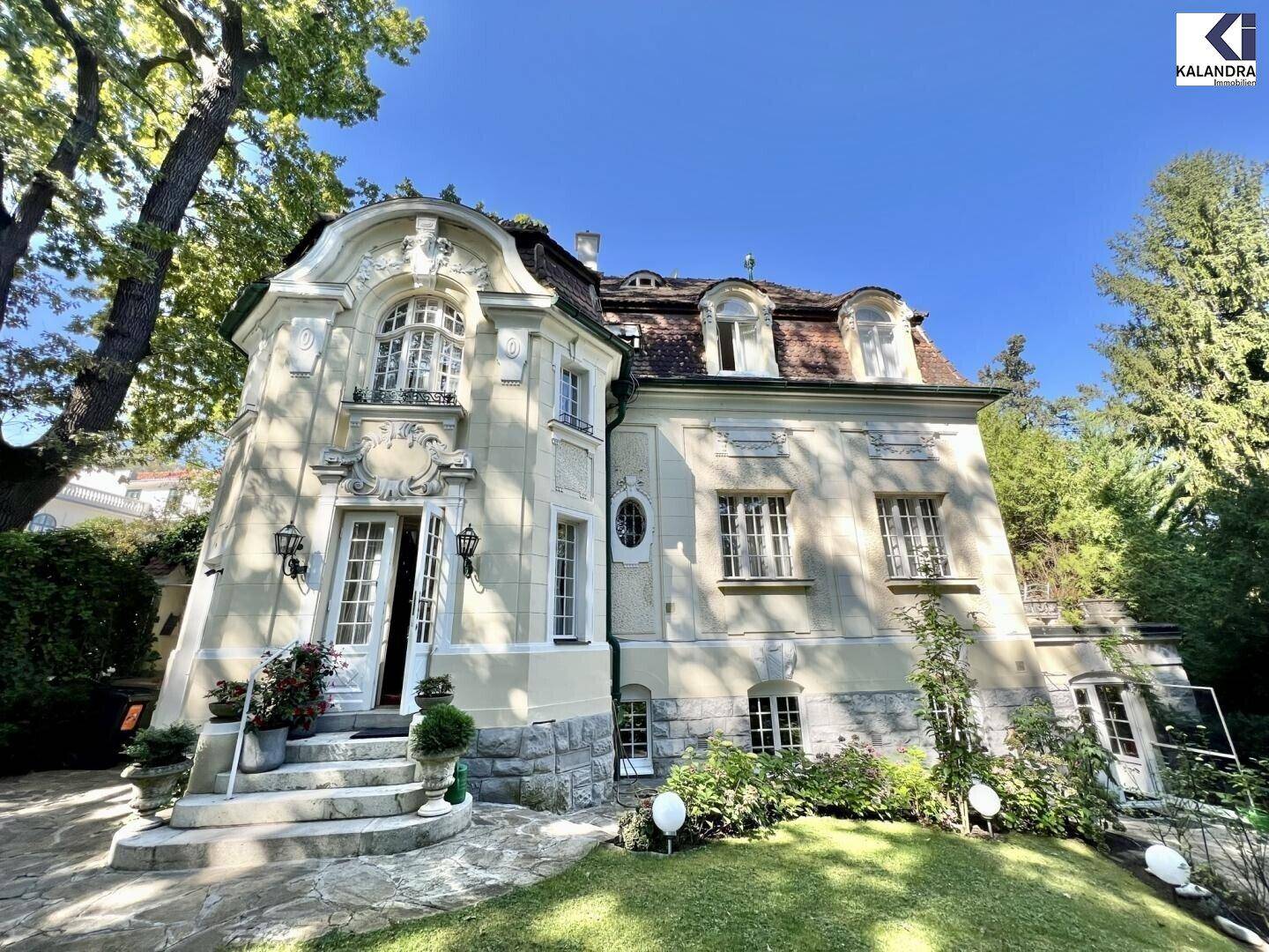 Historische Villa mit aufwendiger Fassade und gepflegtem Vorgarten unter blauem Himmel.