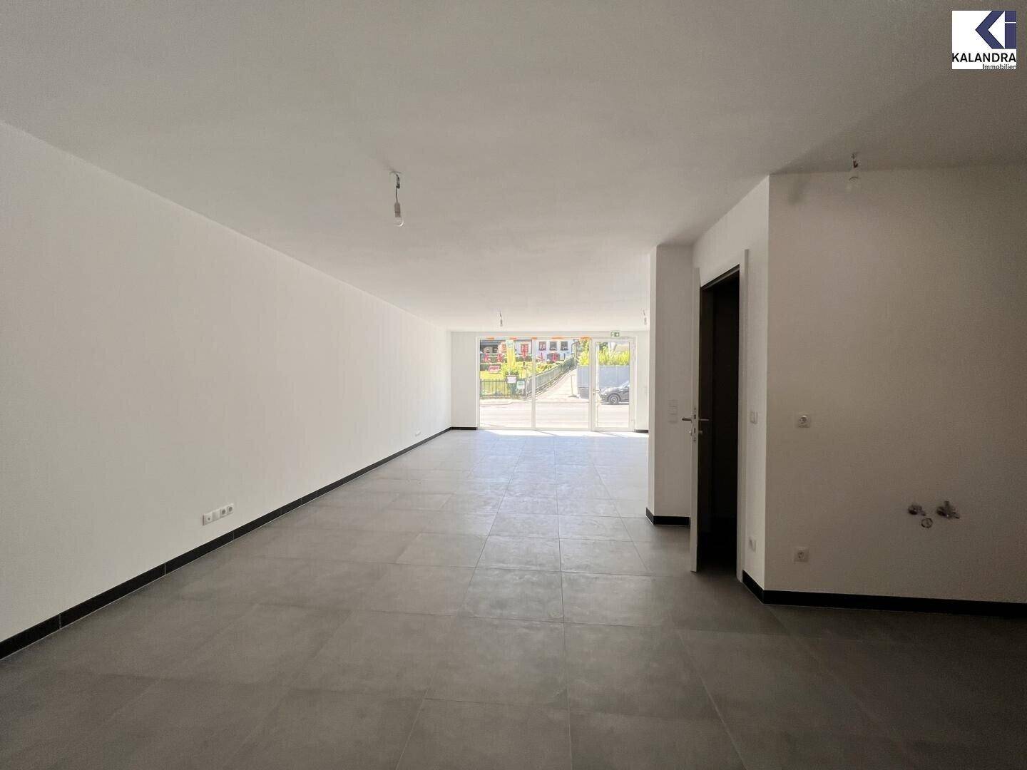 Geräumiger, unmöblierter Innenraum mit hellen Wänden, Fliesenboden und einer Tür im Hintergrund.