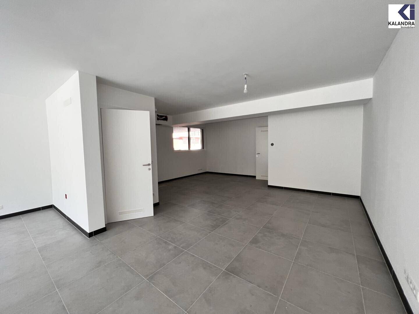 Geräumiger, unmöblierter Innenraum mit hellen Wänden, Fliesenboden und einem Fenster zur Seite.