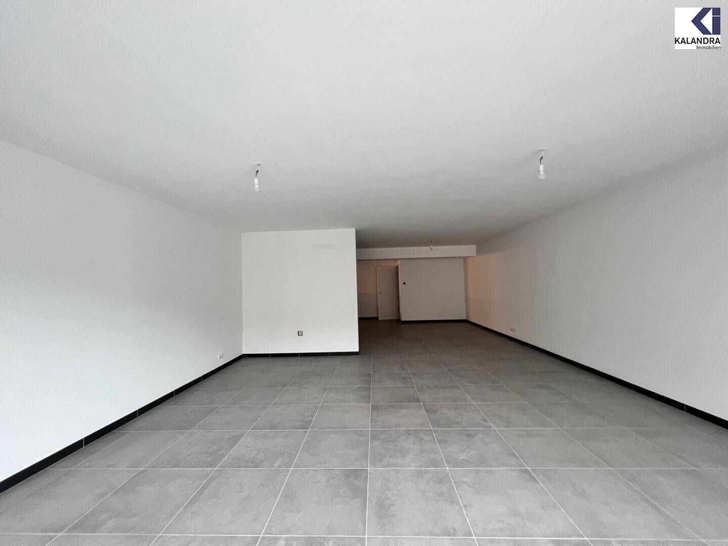 Heller, leerer Raum mit großen Glasfronten zur Straße hin und modernem Fliesenboden.