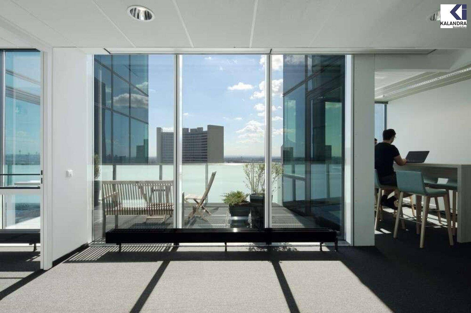 Heller Büroraum mit Teppichboden und Zugang zu einem Balkon oder einer Terrasse mit Stadtblick.