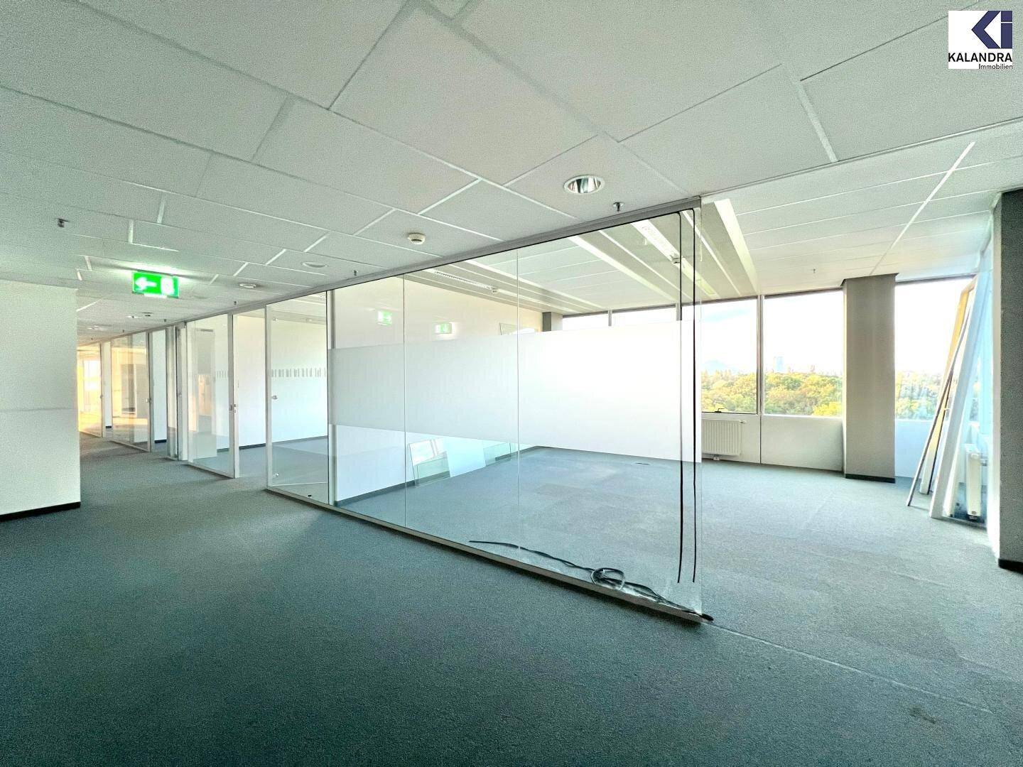 Helles, leeres Büro mit Teppichboden und Glaswänden, die eine offene Raumgestaltung ermöglichen.