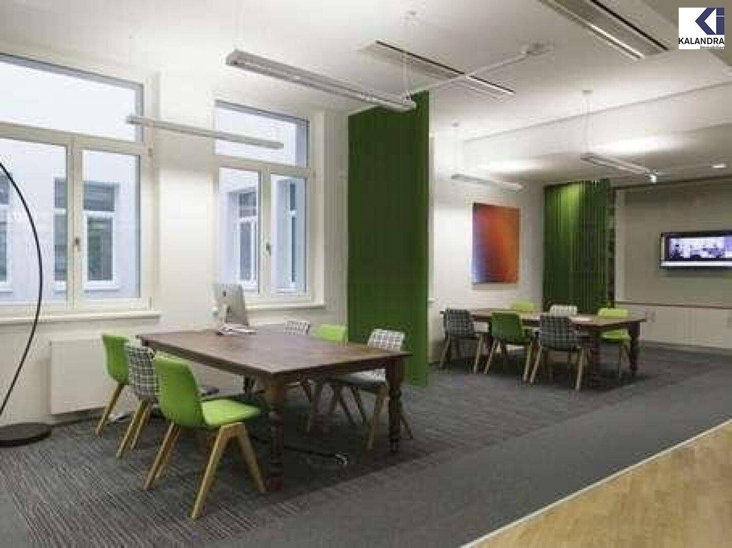Kreativer Besprechungsraum mit Holztischen, grünen Stühlen und Teppichboden, ideal für Teamarbeit.