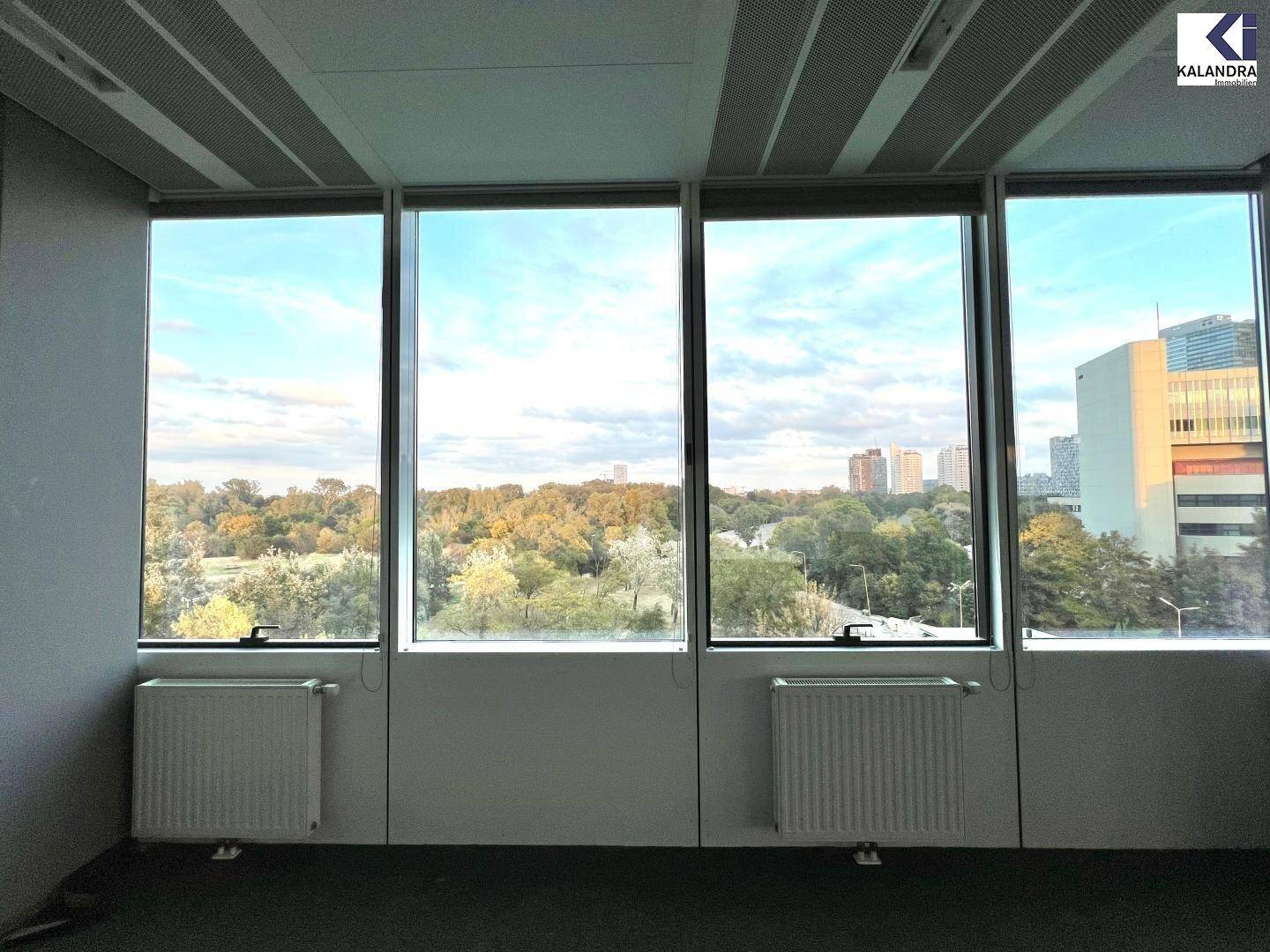 Leeres Büro mit Teppichboden und großen Fenstern, die einen weiten Blick auf die grüne Umgebung bieten.