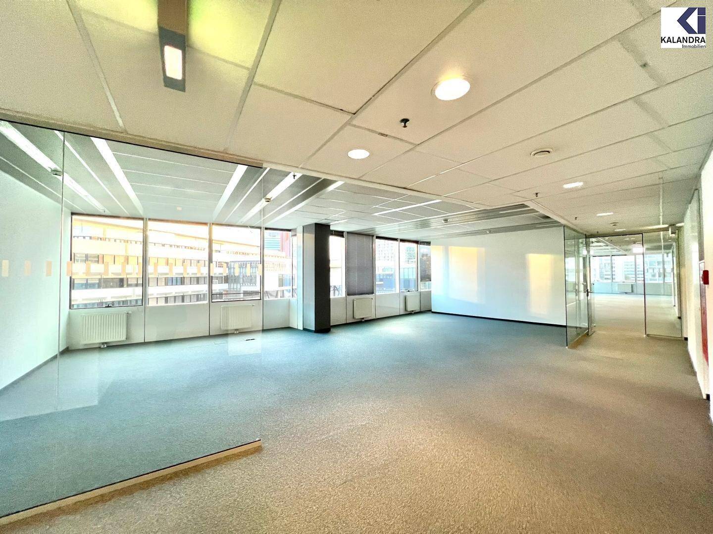 Helles, leeres Büro mit Teppichboden und Glaswänden, die eine offene Raumgestaltung ermöglichen.