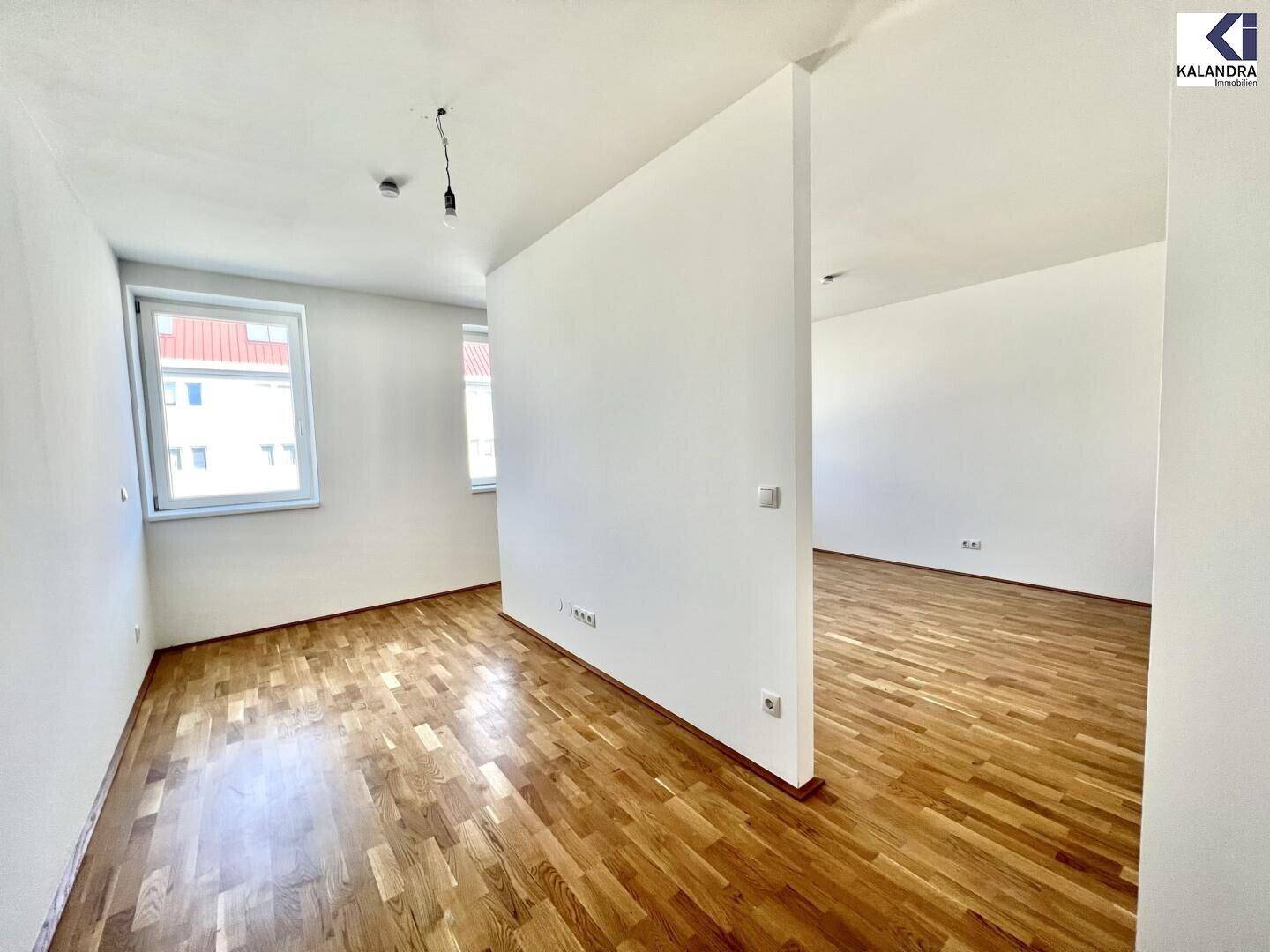 Geräumiger, heller Raum mit Holzboden und einer Trennwand, ideal für flexible Nutzung.