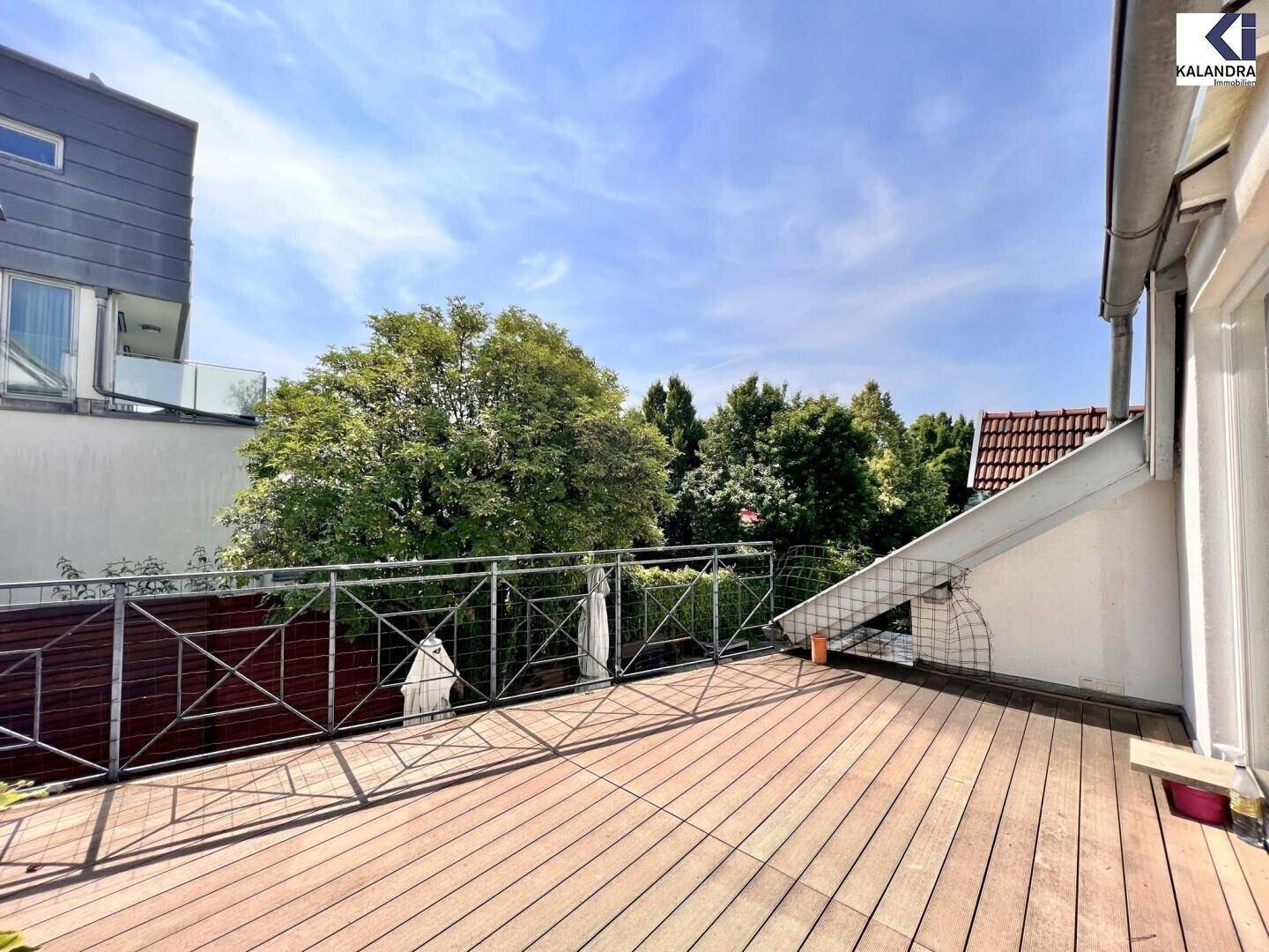 Geräumige Holzterrasse mit Metallgeländer und Blick auf umliegende Bäume.