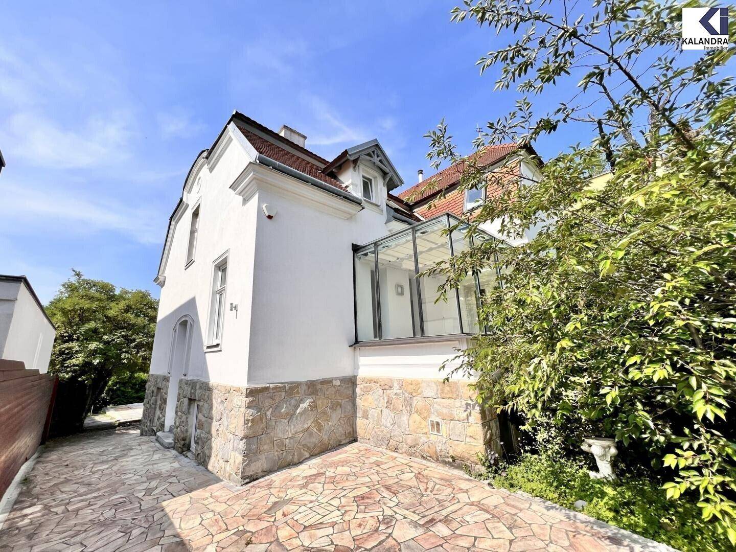 Historisches Gebäude mit weißer Fassade, Steinsockel und Wintergartenanbau.
