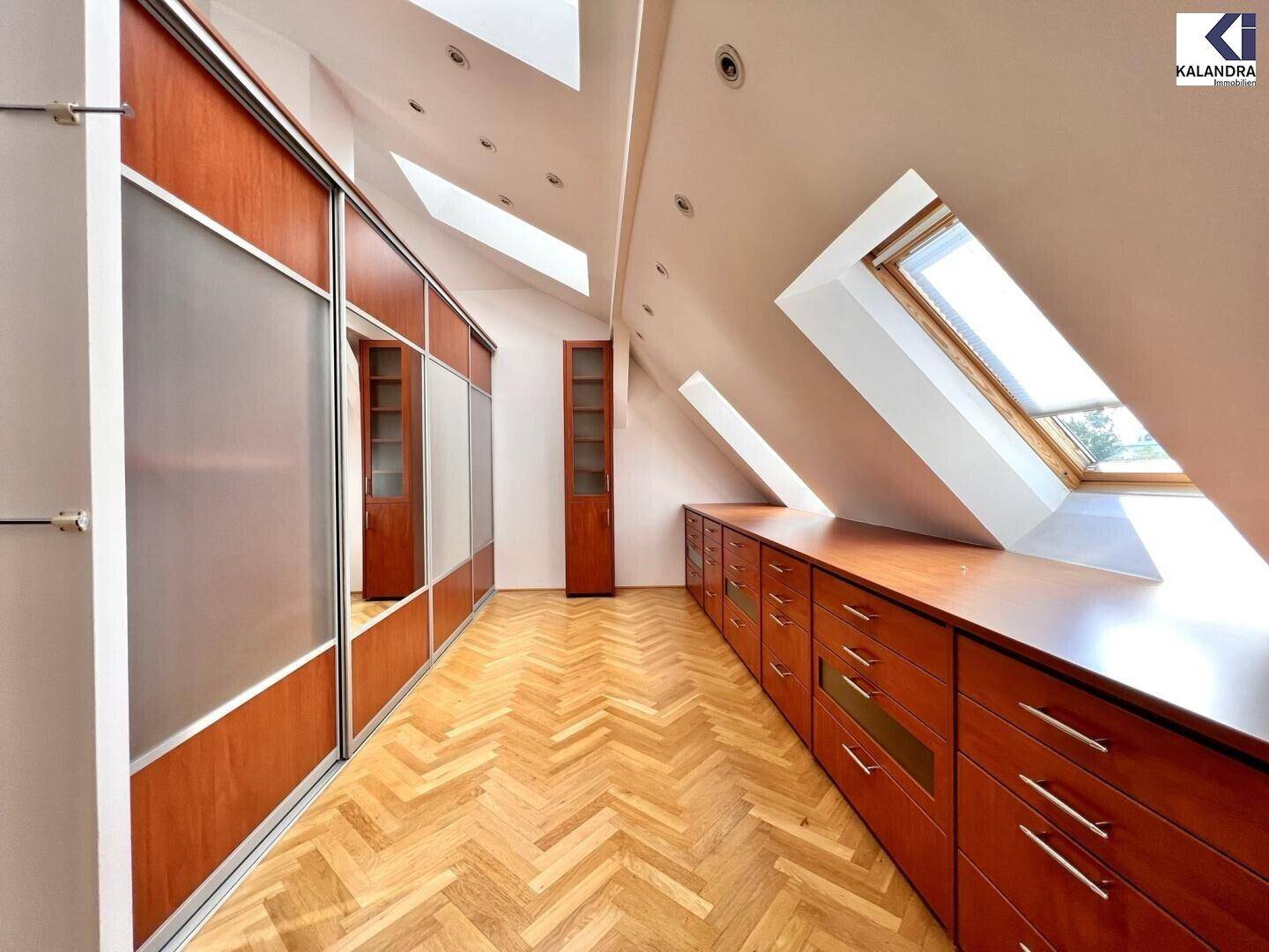 Geräumiger begehbarer Kleiderschrank im Dachgeschoss mit Einbauschränken und Dachfenstern.