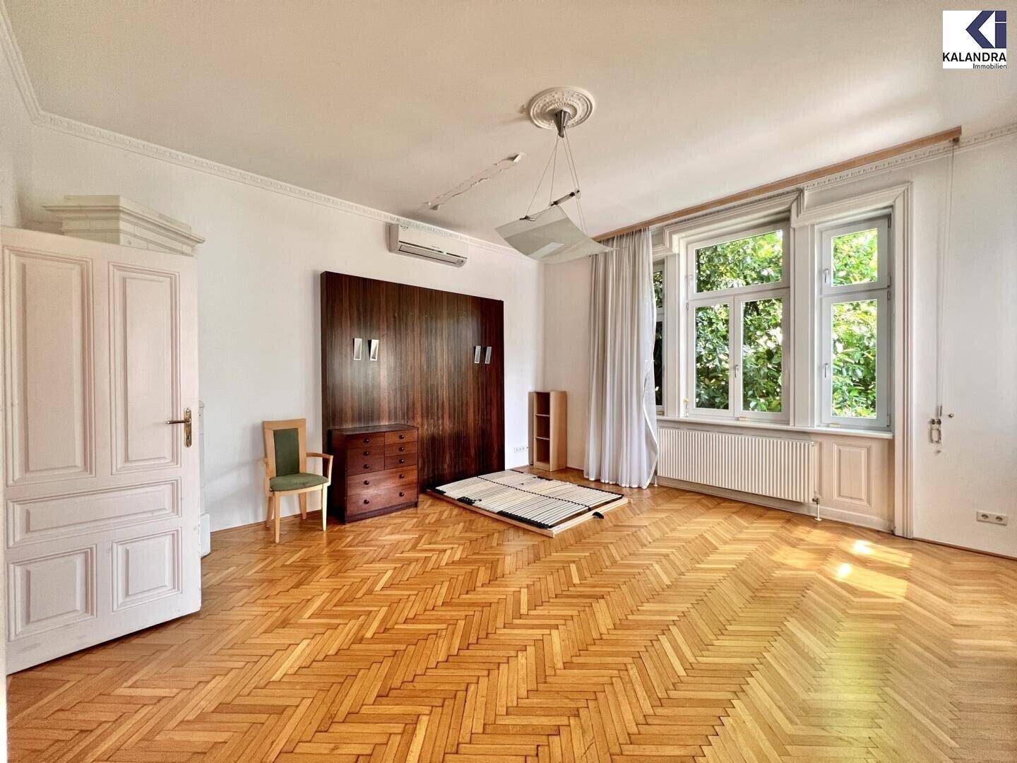 Geräumiges Zimmer mit Fischgrätparkett, hohen Decken und Blick ins Grüne.