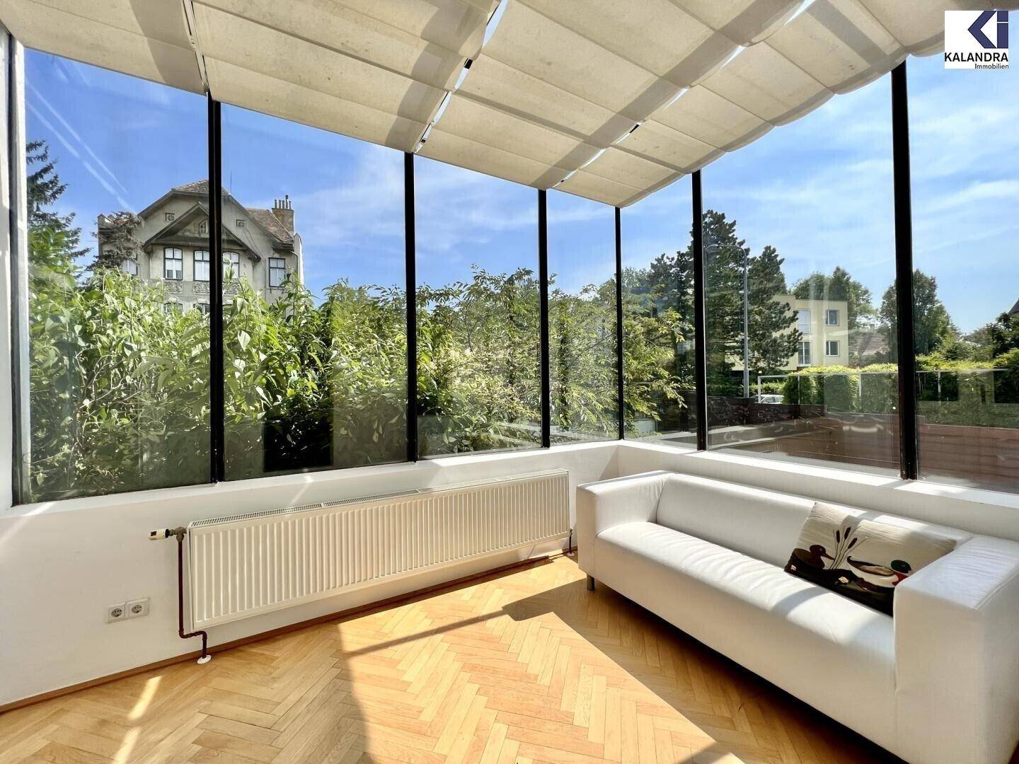 Heller Wintergarten mit großen Glasfronten, Parkettboden und Blick ins Grüne.