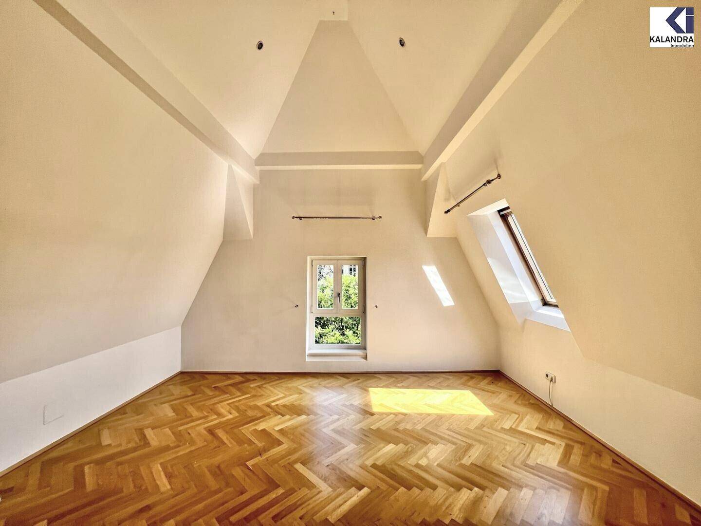 Helles Zimmer im Dachgeschoss mit Parkettboden, hohen Decken und Dachfenstern.