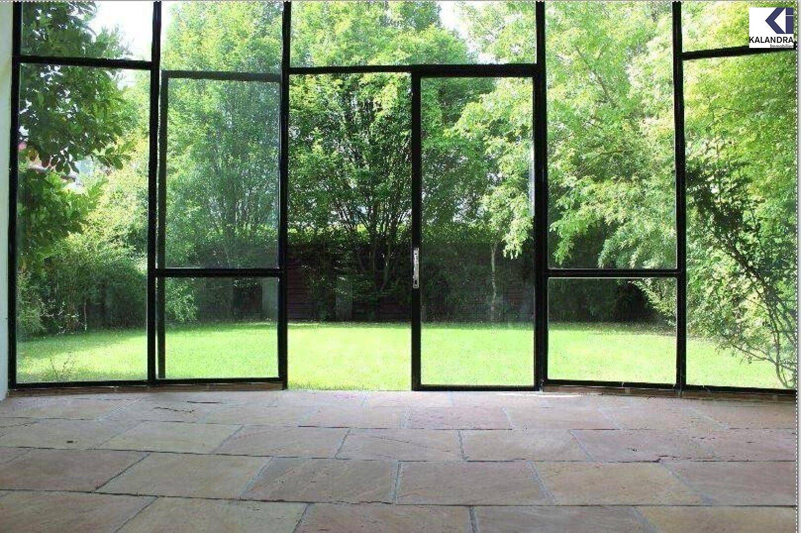 Heller Wintergarten mit großen Glasfronten und direktem Blick in den Garten.