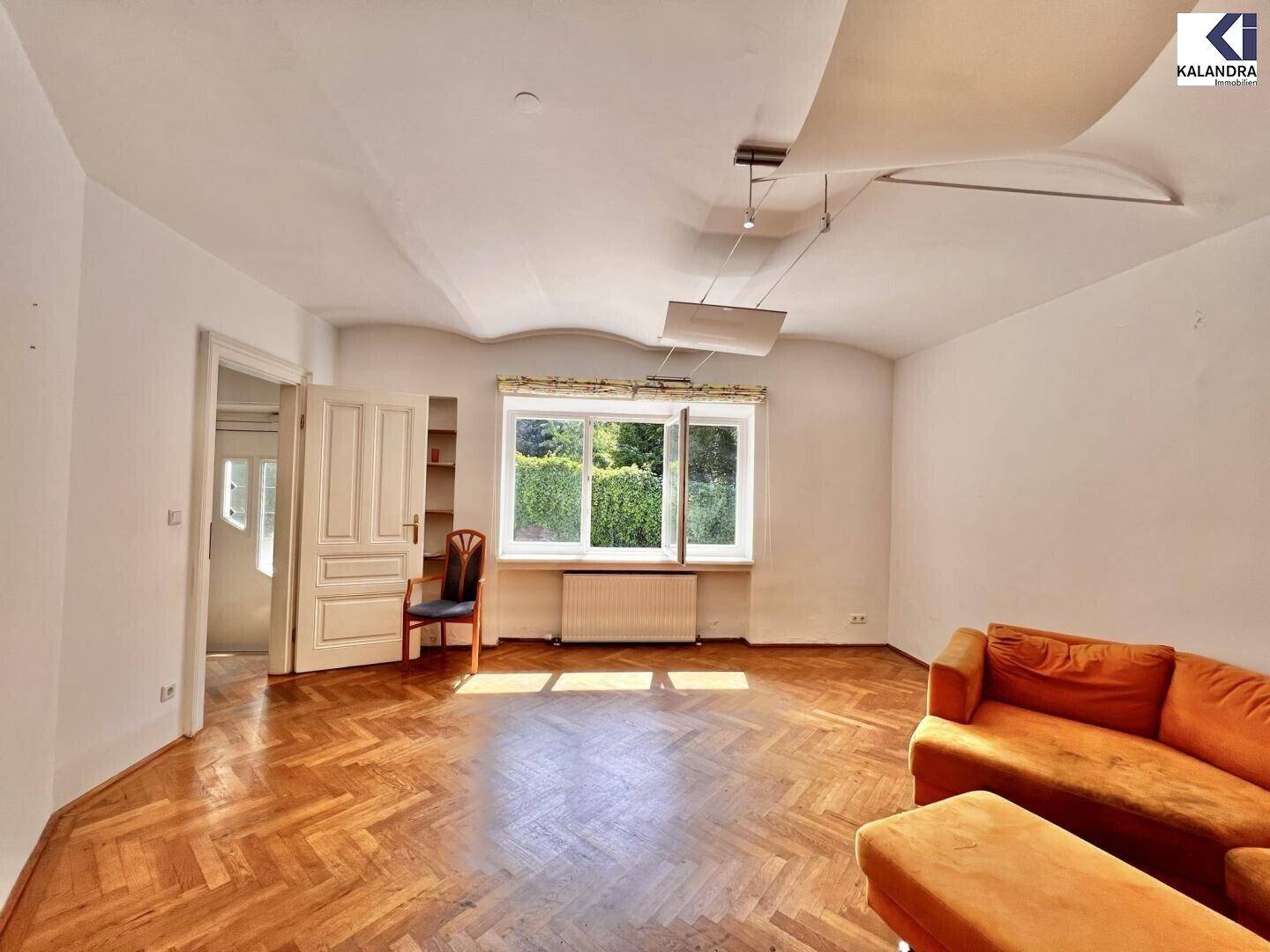 Helles Wohnzimmer mit Parkettboden, Sofa und Blick in den grünen Garten.