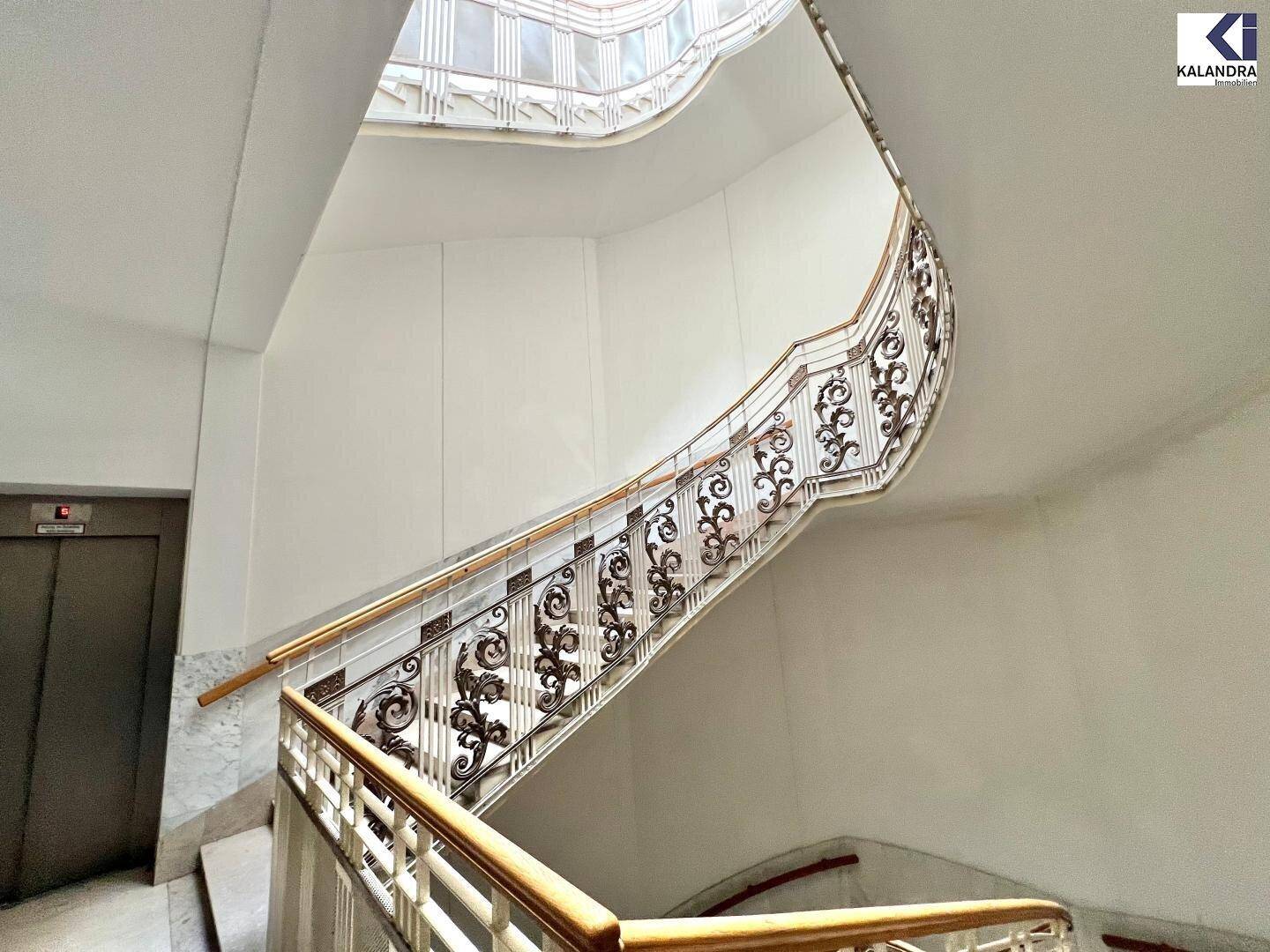 Elegantes Treppenhaus mit kunstvollem Geländer, Marmorstufen und Aufzug.