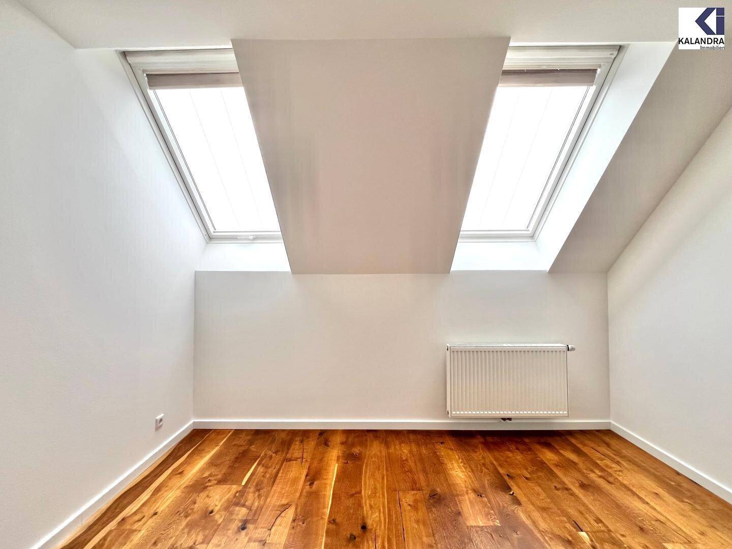 Heller Raum im Dachgeschoss mit Holzboden, zwei Dachfenstern und weiß gestrichenen Wänden.