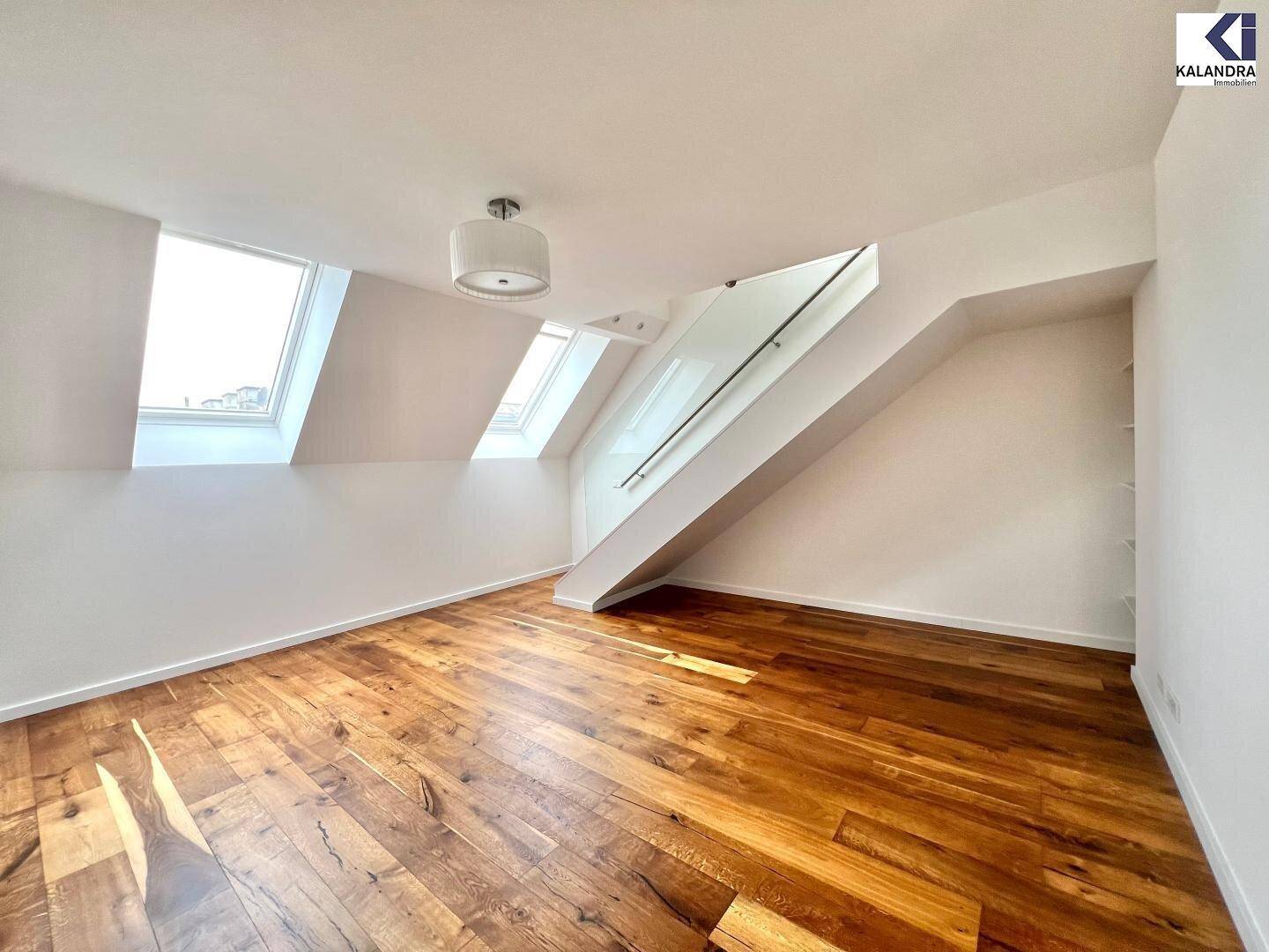 Heller Raum mit Holzboden, Dachfenstern und einer modernen Treppe mit Glasgeländer.