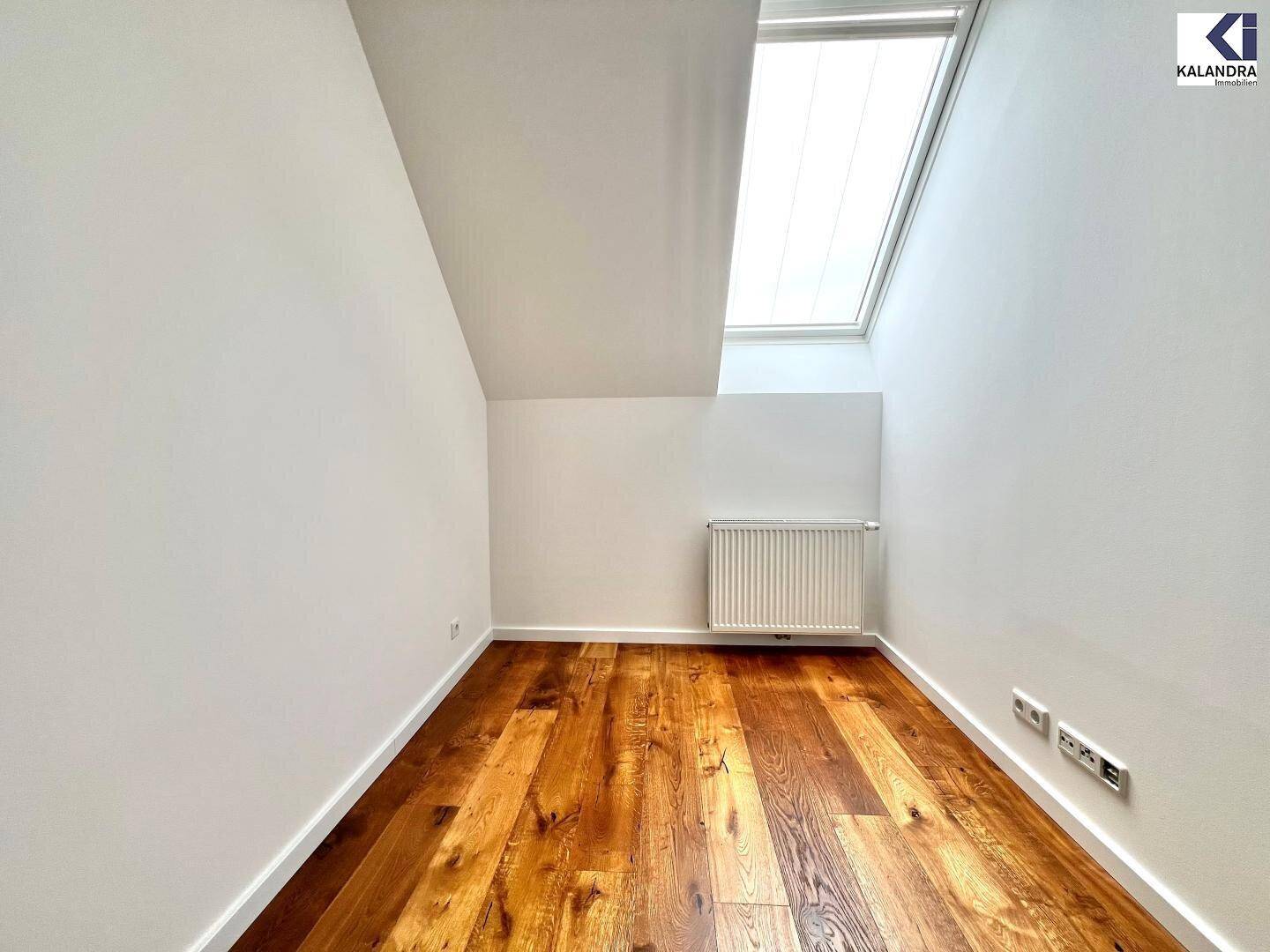 Kleiner, heller Raum im Dachgeschoss mit Holzboden, Dachfenster und Heizkörper.