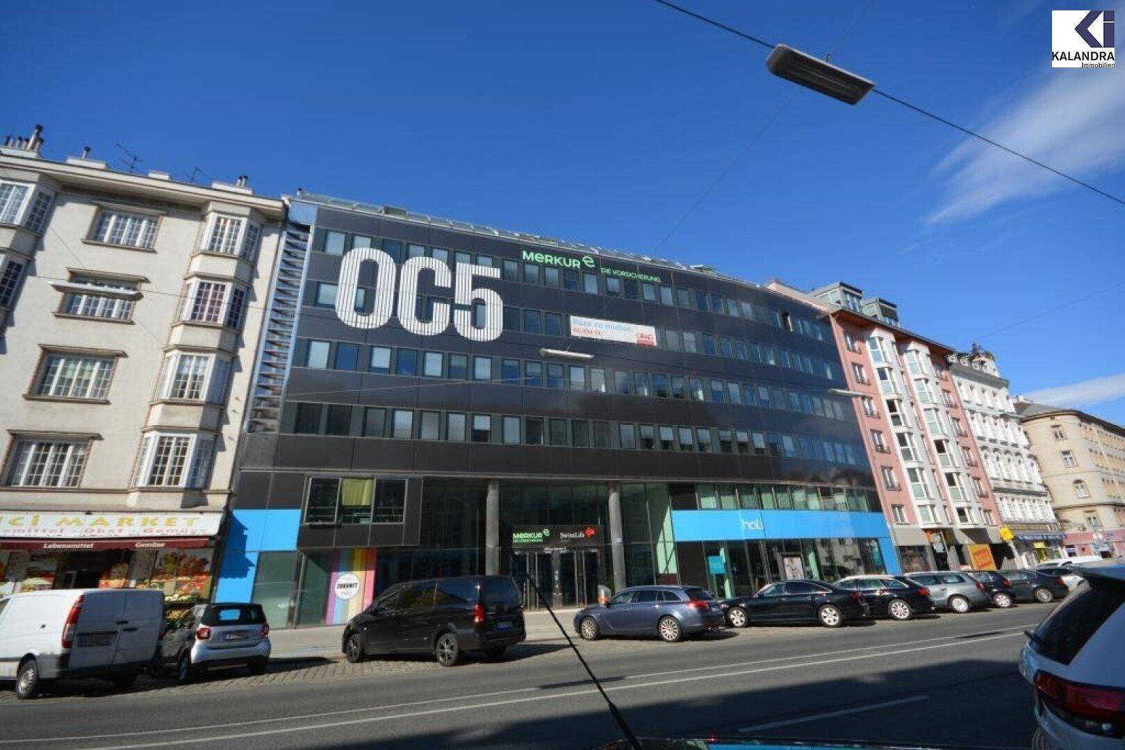 Weitläufige Ansicht eines modernen Bürogebäudes an einer belebten Straße mit parkenden Autos.