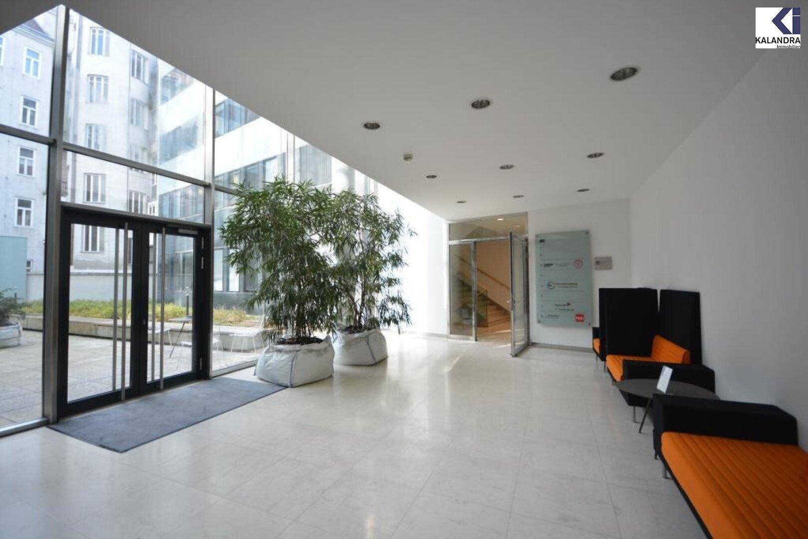 Helle Lobby mit großen Glasfronten, Pflanzen und Sitzgelegenheiten, die einen Blick in den Innenhof bietet.