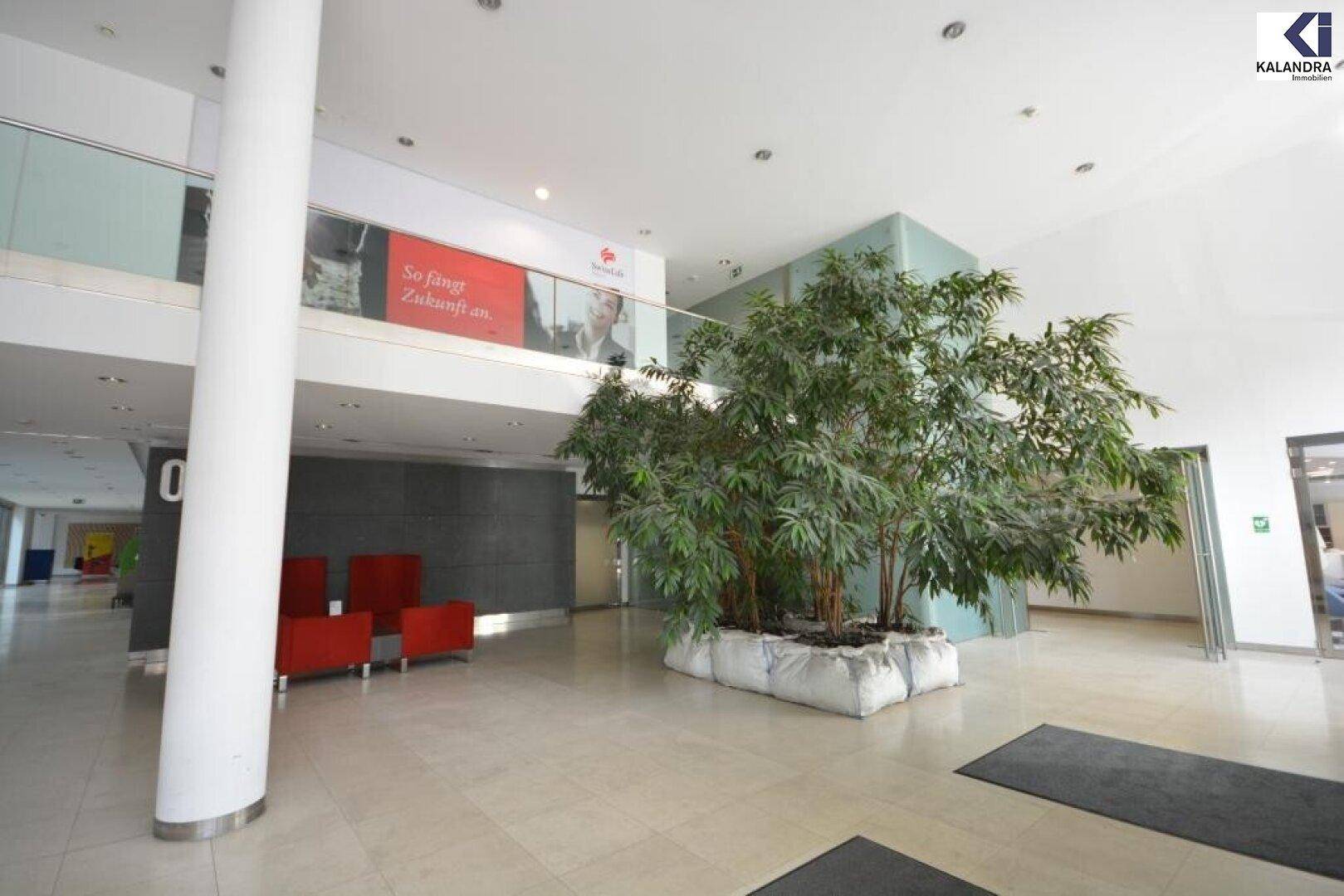 Helle und geräumige Lobby mit hohen Decken, Pflanzen und roten Sitzgelegenheiten.