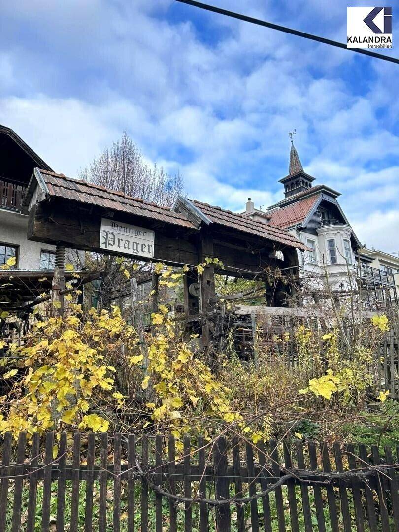 Historisches Gebäude mit traditioneller Architektur, umgeben von herbstlicher Vegetation und einem Holzzaun.