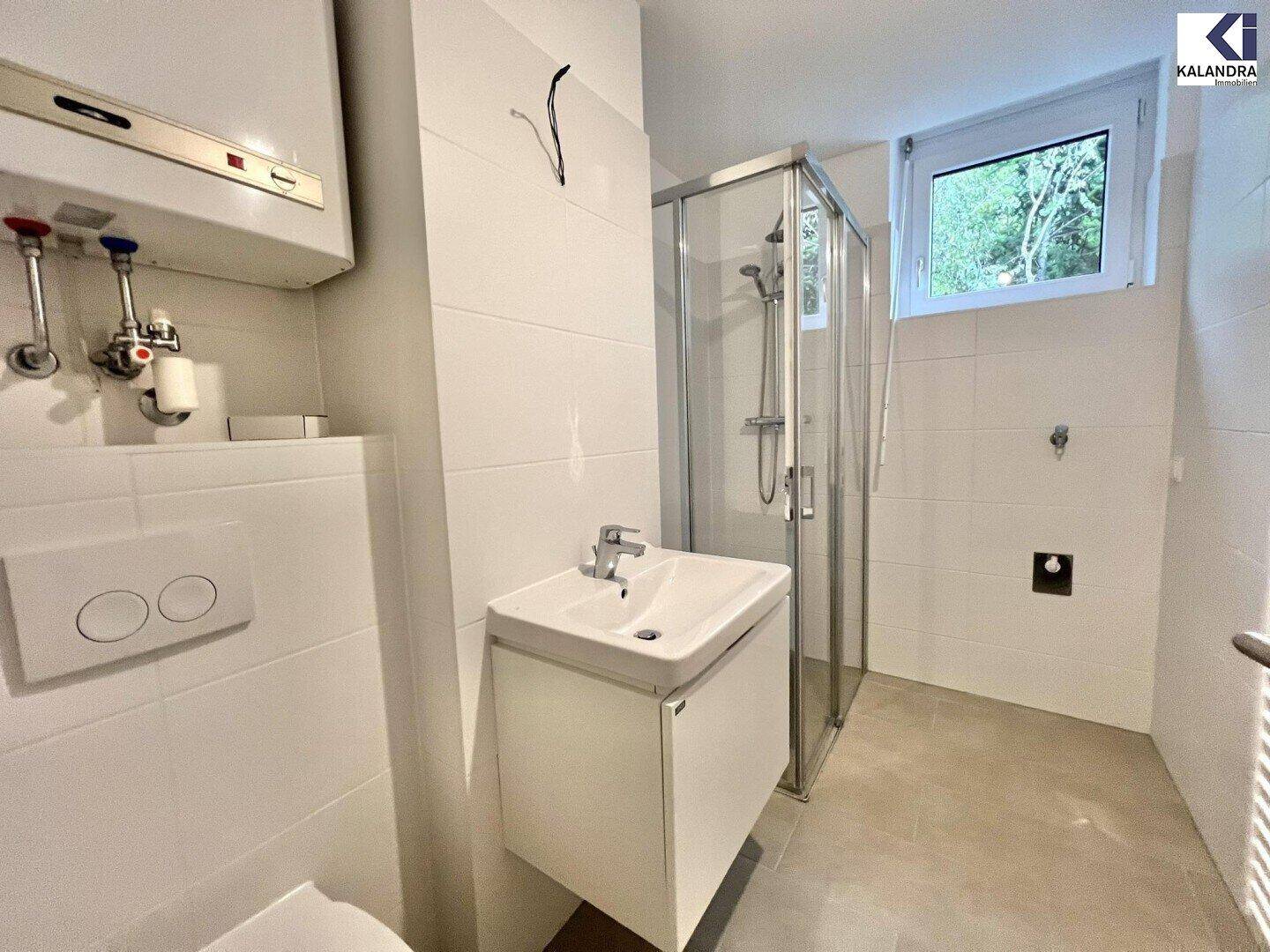 Modernes Badezimmer mit weißen Fliesen, Duschkabine, Waschbecken, wandhängendem WC und Fenster.