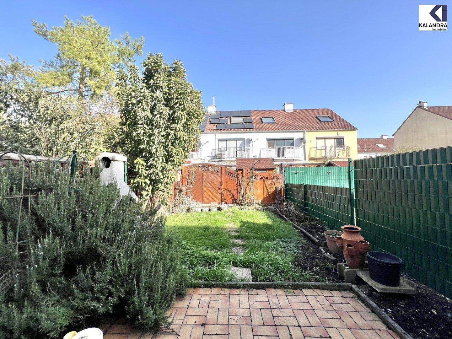 Gepflegter Gartenbereich mit Rasenfläche und gepflasterter Terrasse hinter dem Haus.