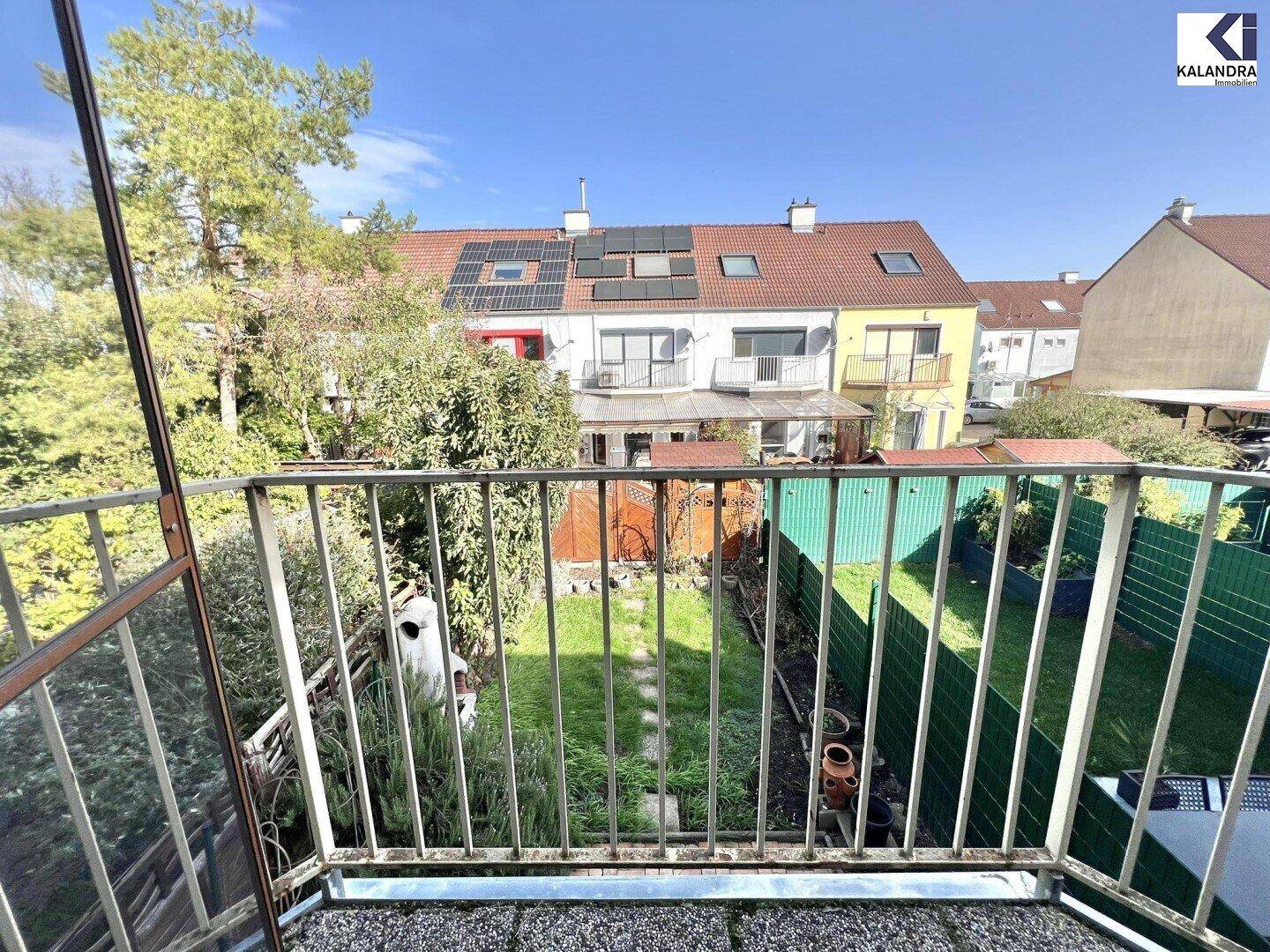 Blick vom Balkon auf die grünen Gärten und die umliegenden Reihenhäuser.