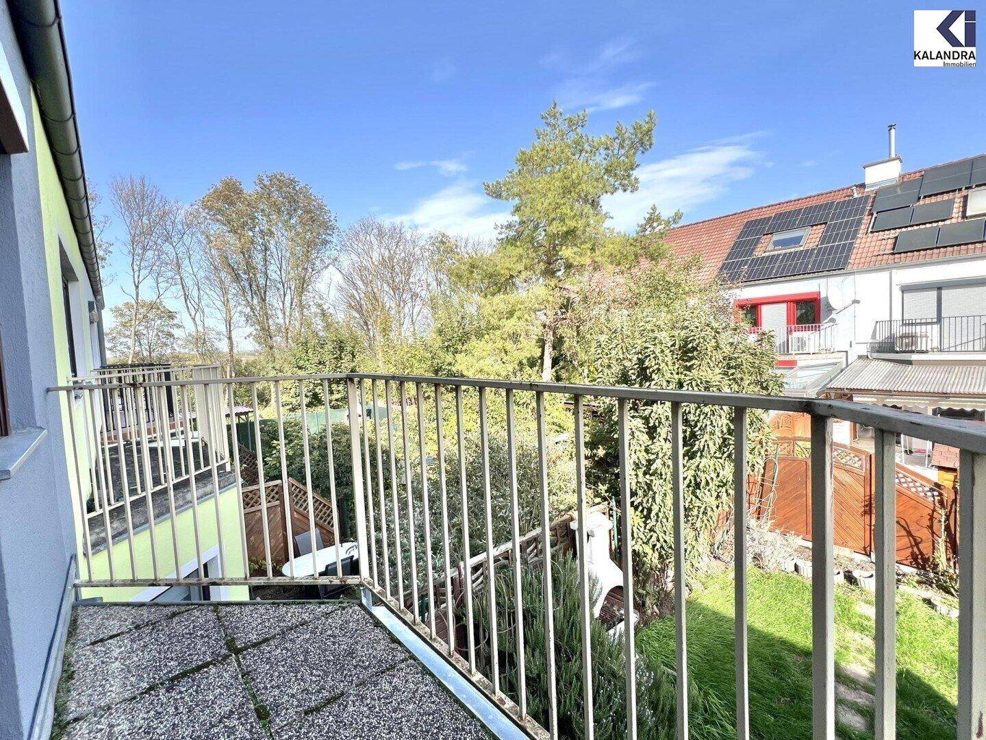 Weiter Blick vom Balkon ins Grüne mit Bäumen und benachbarten Häusern.