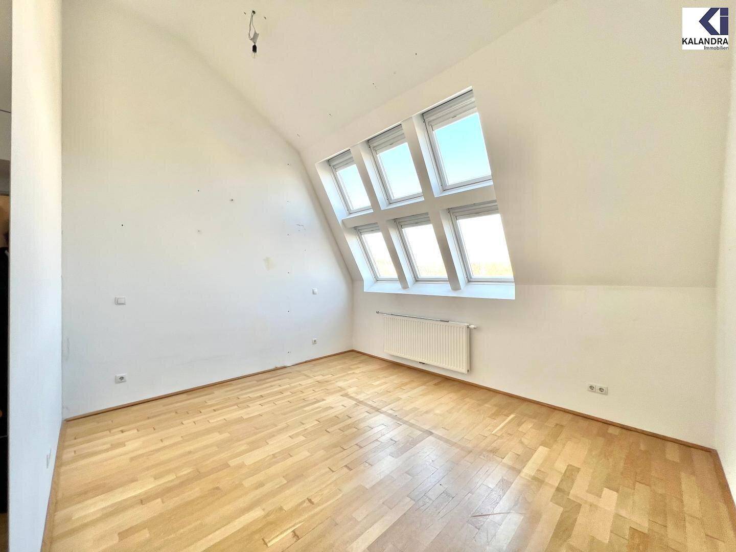 Helles Zimmer im Dachgeschoss mit Holzboden, schrägen Wänden und großen Dachfenstern.